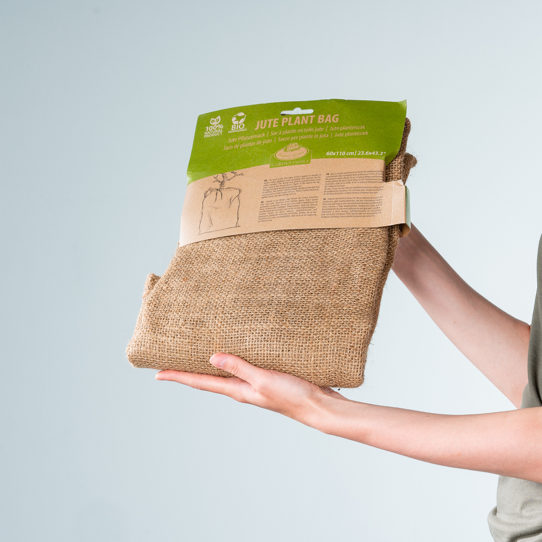 Das Bild zeigt die Hände einer Person, die vor dem Hintergrund eines klaren Himmels einen Jute-Pflanzsack mit einem grünen Etikett hält.