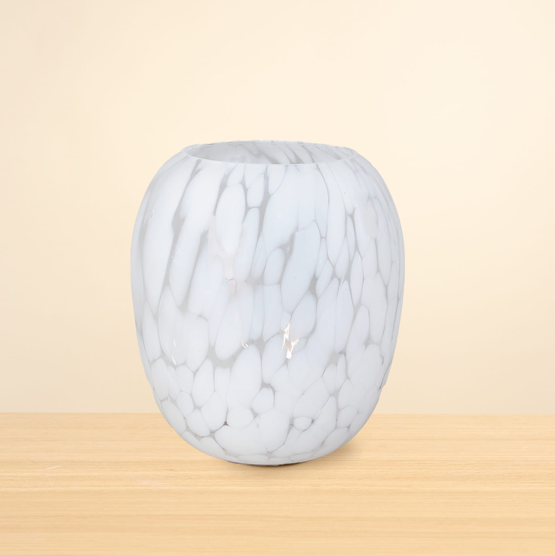 Eine weiße, marmorähnliche Vase oder ein Behälter steht auf einer Holzoberfläche vor einem hellen Hintergrund.