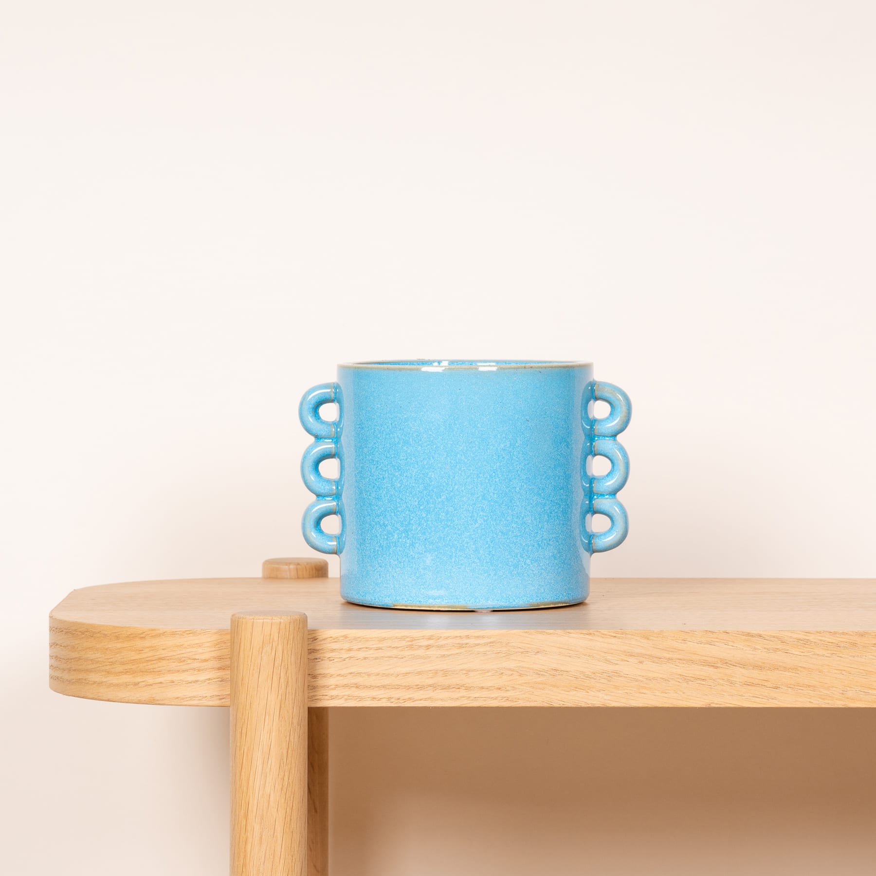 Eine blaue Keramiktasse mit gewelltem Rand steht auf einer Holzoberfläche vor einem schlichten Hintergrund.