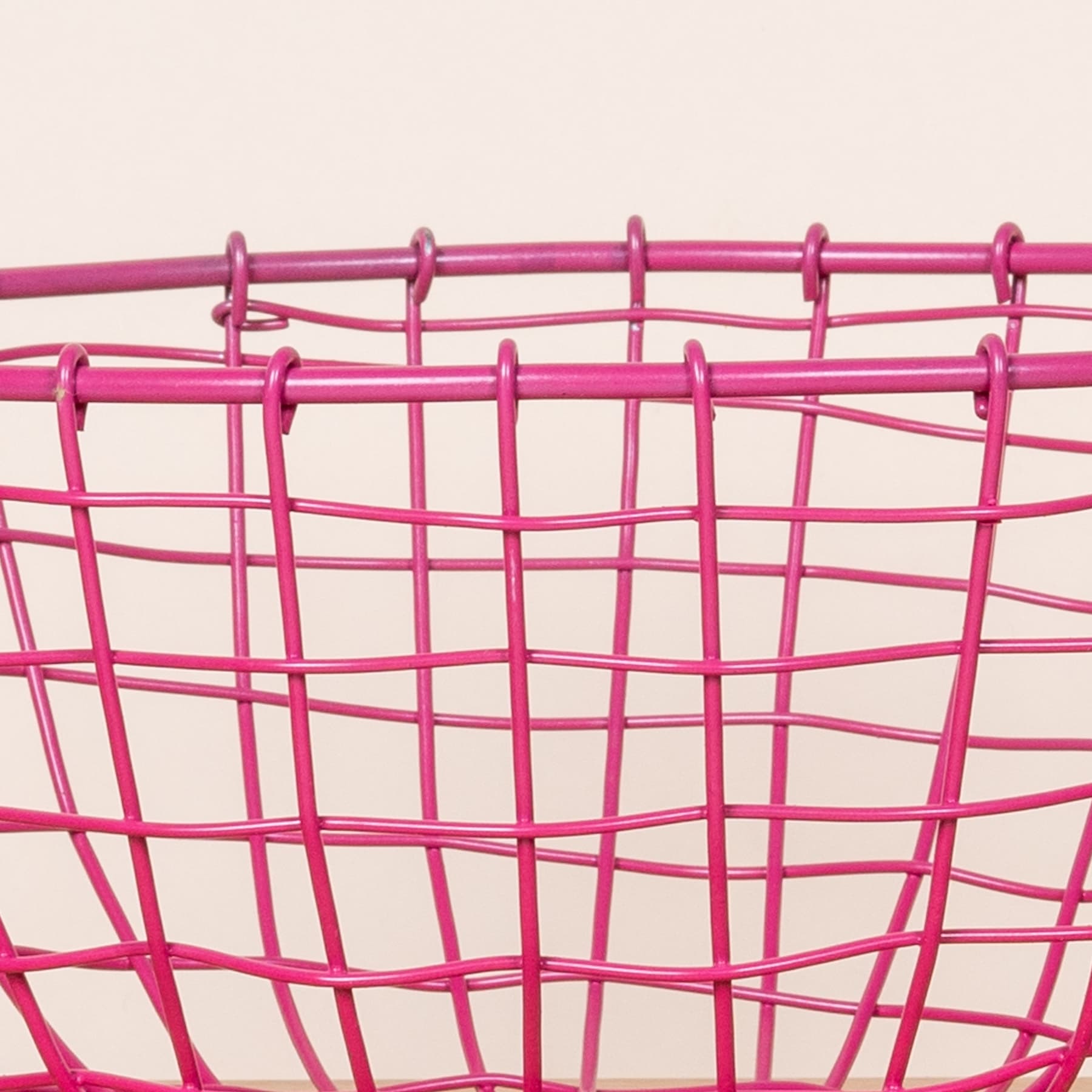 Ein leuchtend rosa Drahtgeflechtkorb oder -behälter mit einem geometrischen, gitterartigen Muster auf einem schlichten, hellen Hintergrund.