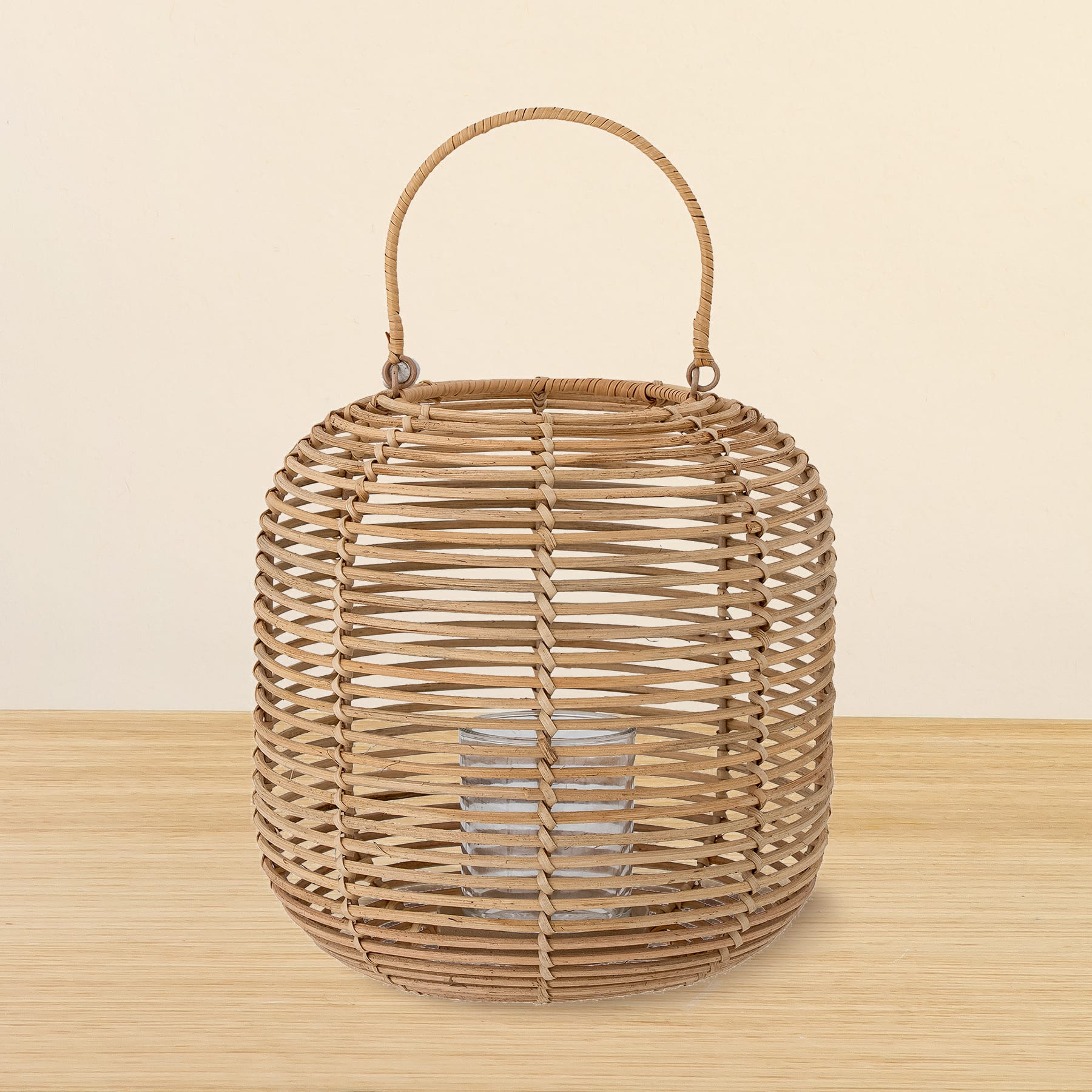 Eine geflochtene Rattanlaterne mit Griff steht auf einer Holzoberfläche vor einem schlichten beigen Hintergrund.