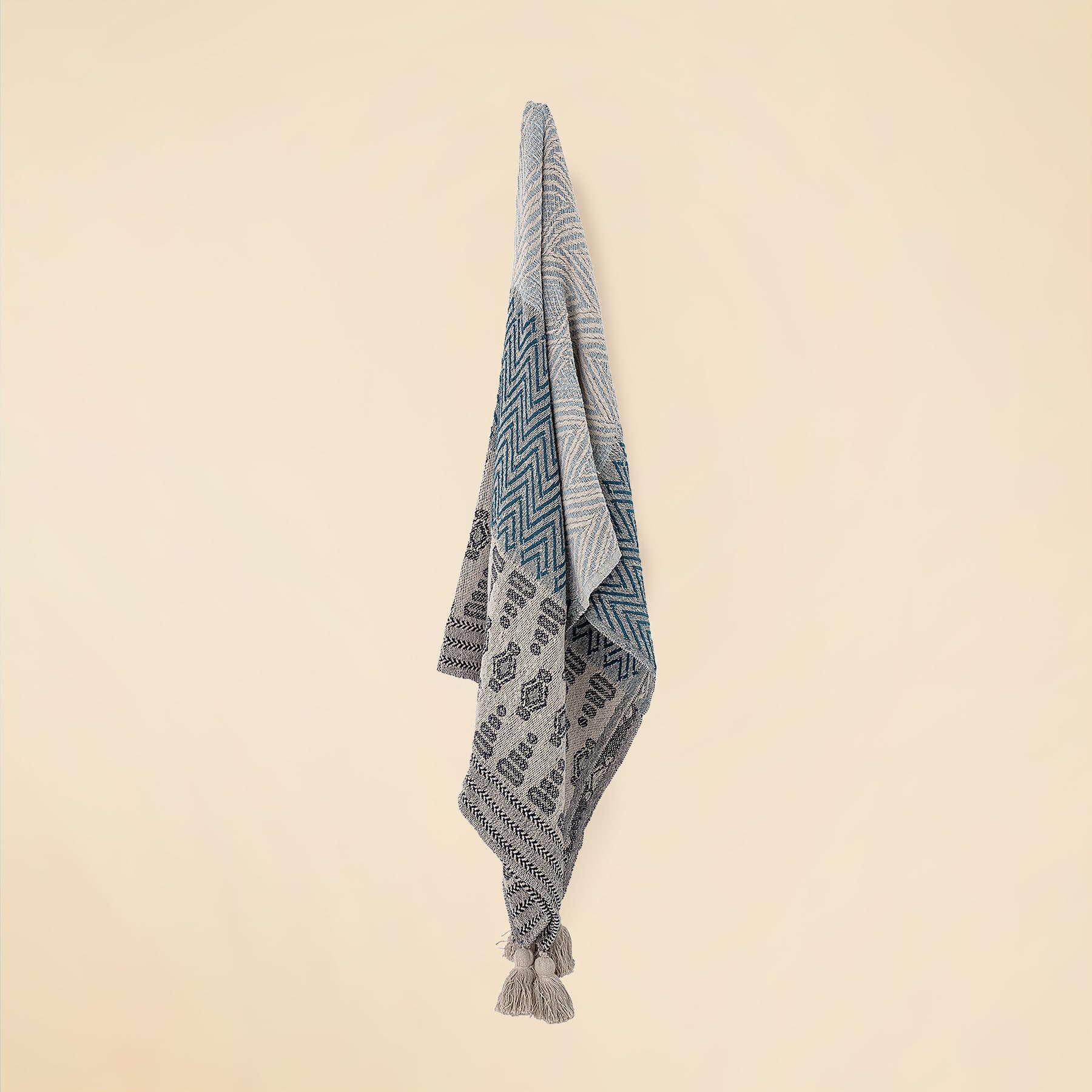 Vor einem hellbeigen Hintergrund hängt ein grau-weiß gemusterter Textil, möglicherweise ein Handtuch oder eine Decke.