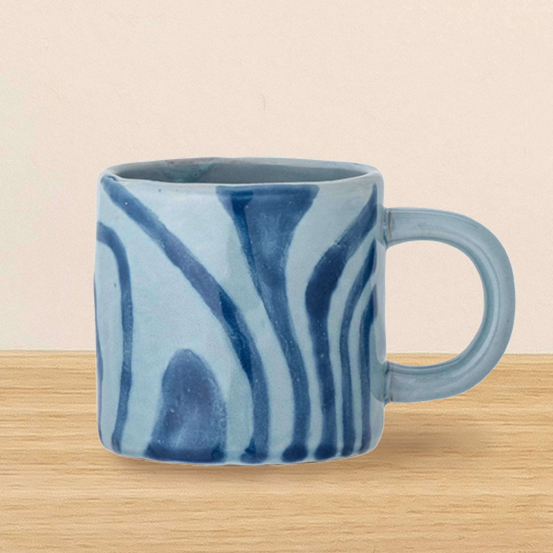 Eine blau-weiße Keramiktasse mit Wirbelmuster steht auf einer Holzoberfläche vor einem hellen Hintergrund.