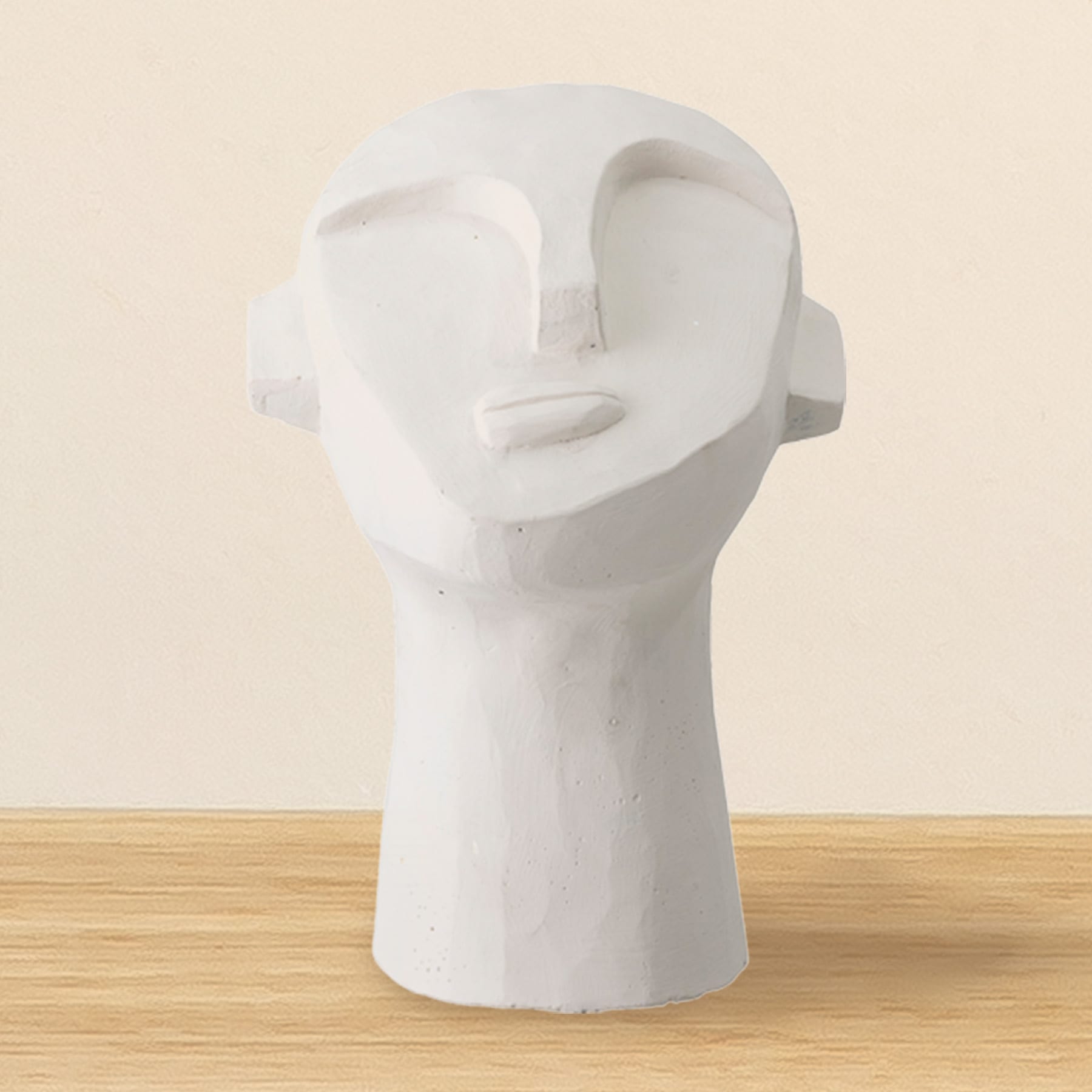 Eine weiße, abstrakte Skulptur eines menschlichen Kopfes ruht auf einer Holzoberfläche vor einem schlichten, beigen Hintergrund.