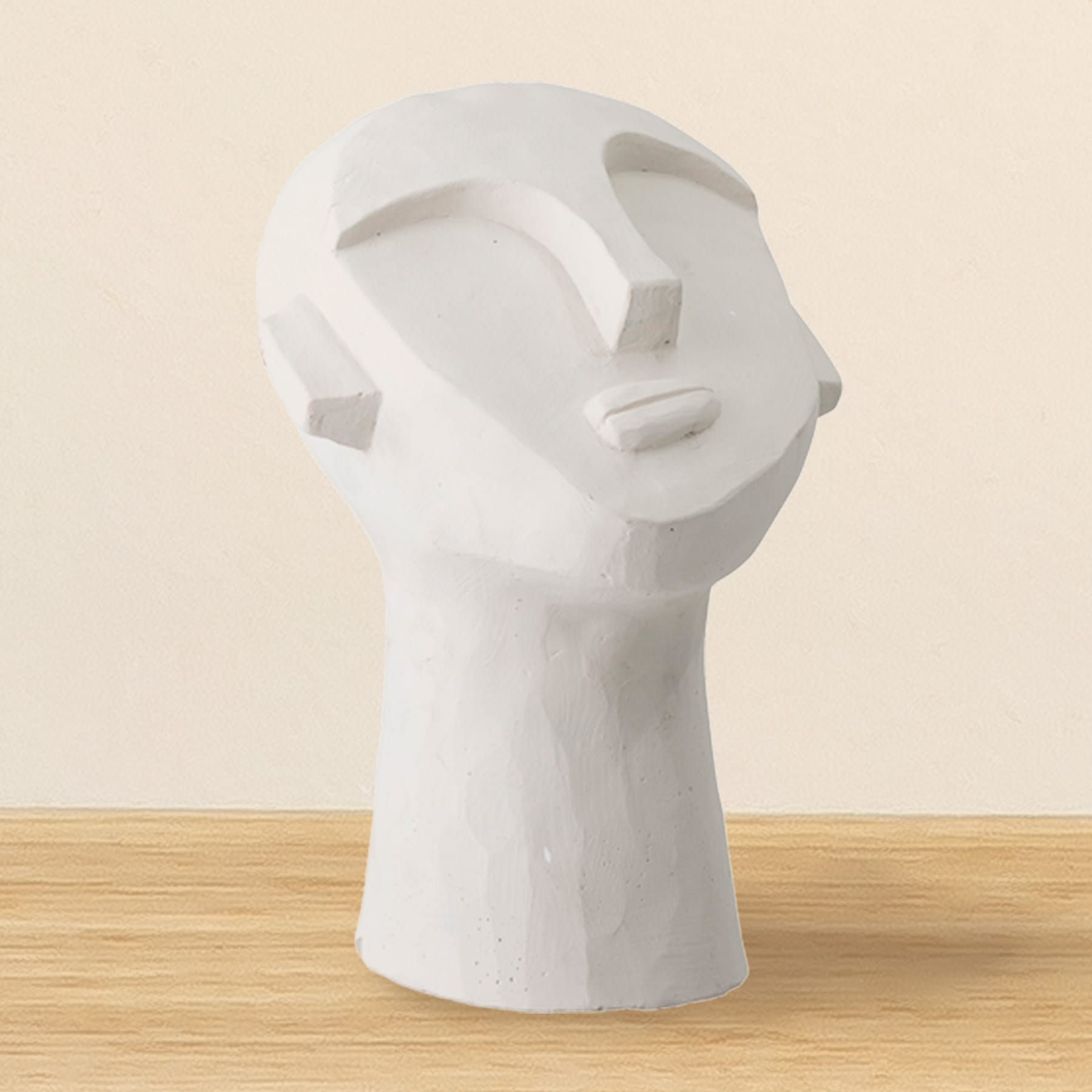 Eine weiße, abstrakte Skulptur eines menschlichen Kopfes ruht auf einer Holzoberfläche vor einem schlichten, beigen Hintergrund.