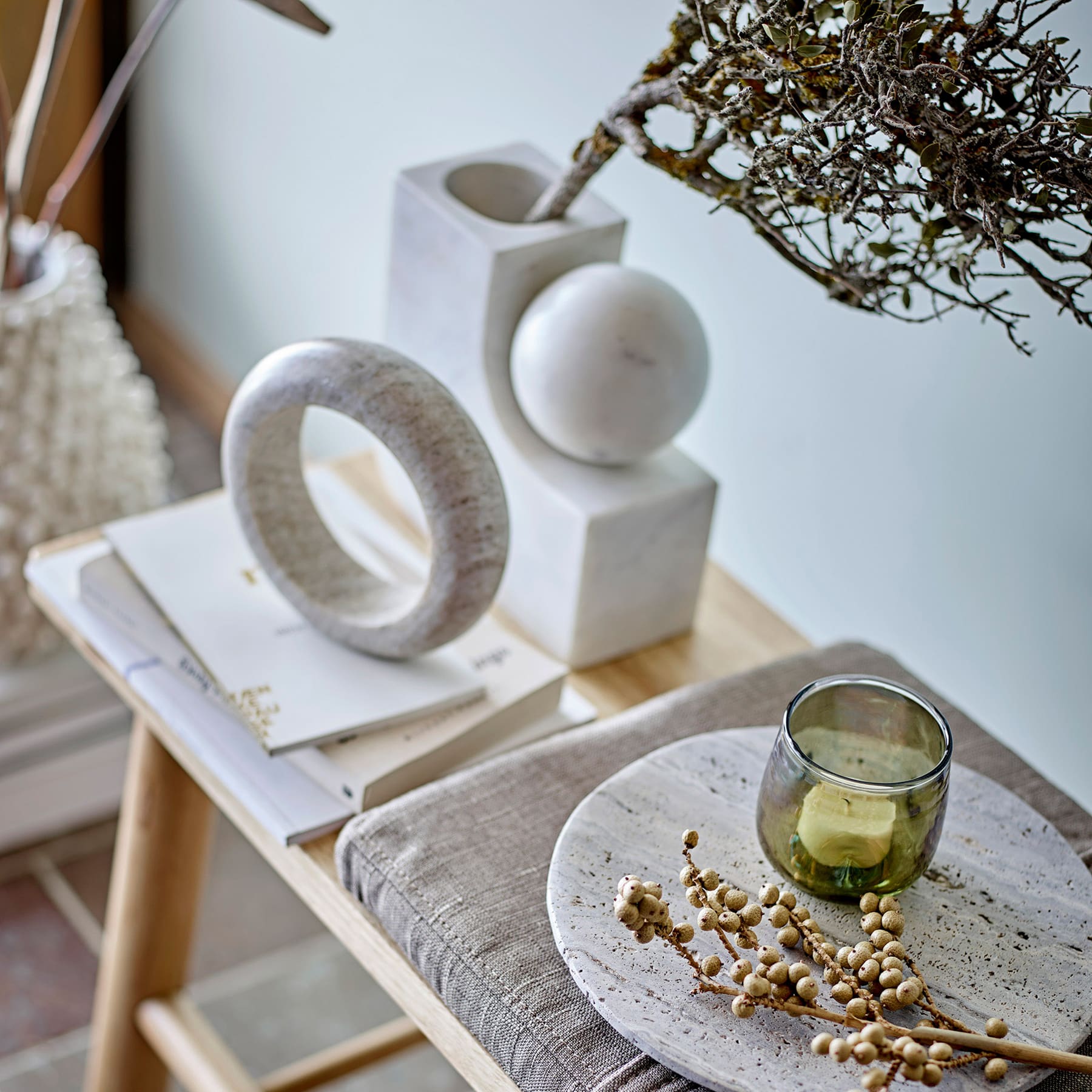 Ein minimalistisches Stillleben-Arrangement mit verschiedenen geometrischen Formen, darunter ein ringförmiges Objekt, eine Kugel und ein Glas mit einer grünen Flüssigkeit, vor einem neutralen Hintergrund mit einem astähnlichen Element.