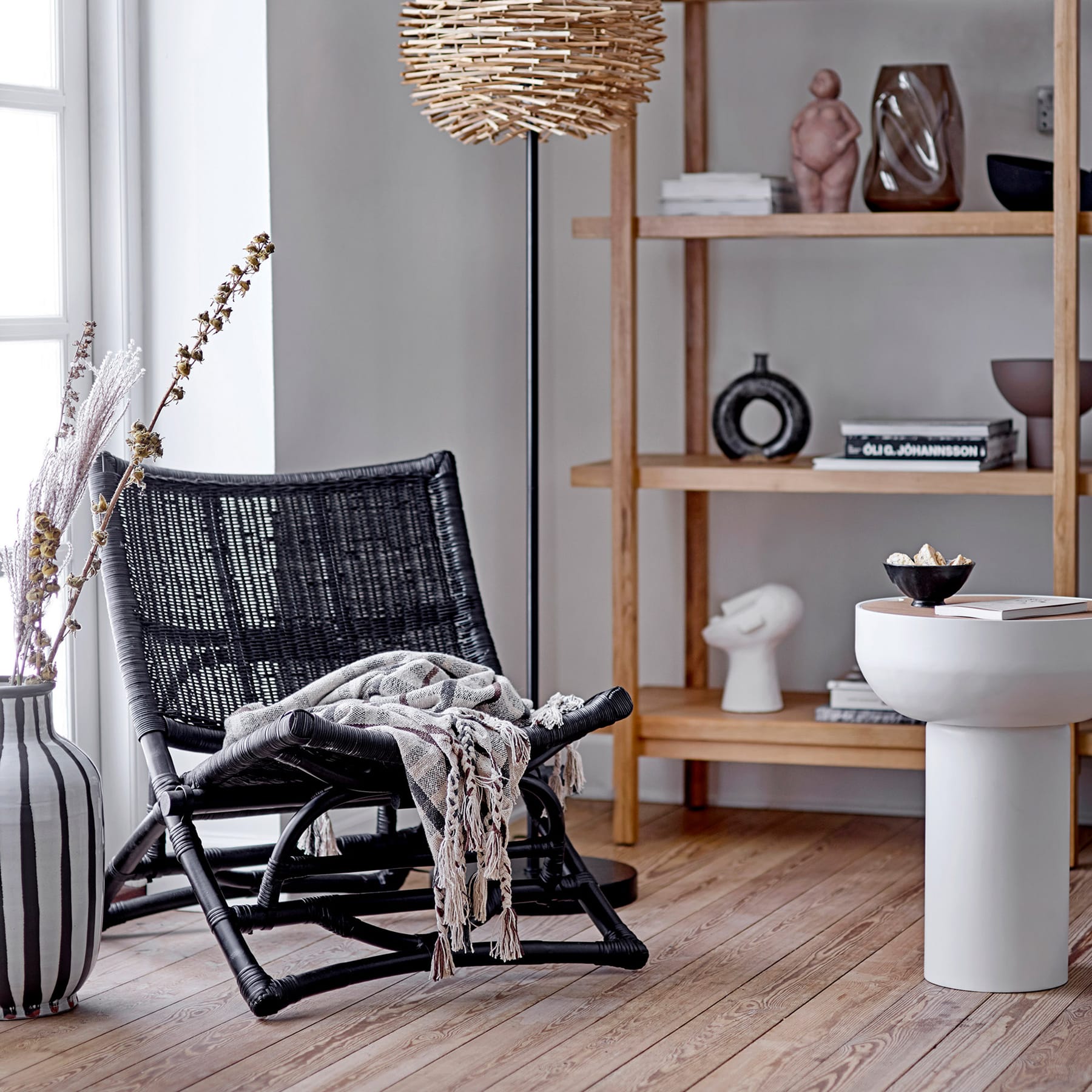 Ein gemütliches und stilvolles Wohnzimmer mit einem geflochtenen Sessel, einem Holzregal mit verschiedenen Dekoartikeln und einer großen Hängelampe, die eine warme und einladende Atmosphäre schafft.