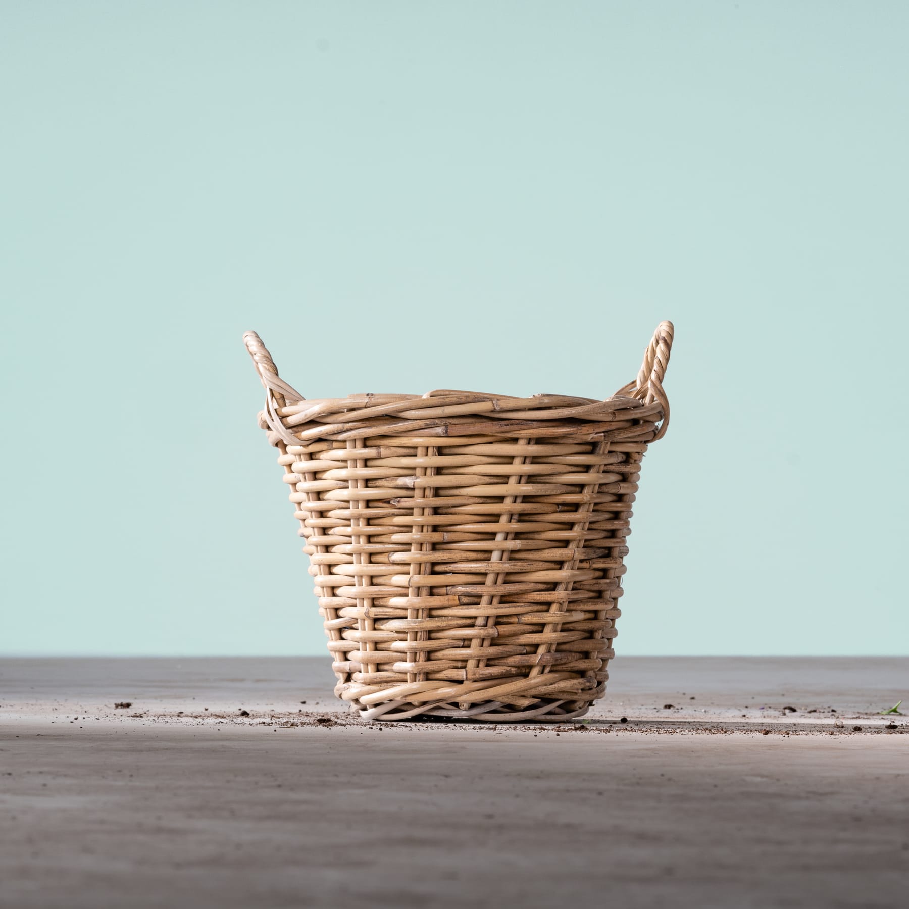 Ein geflochtener Weidenkorb steht auf einer dunklen Holzoberfläche vor einem hellblaugrünen Hintergrund.
