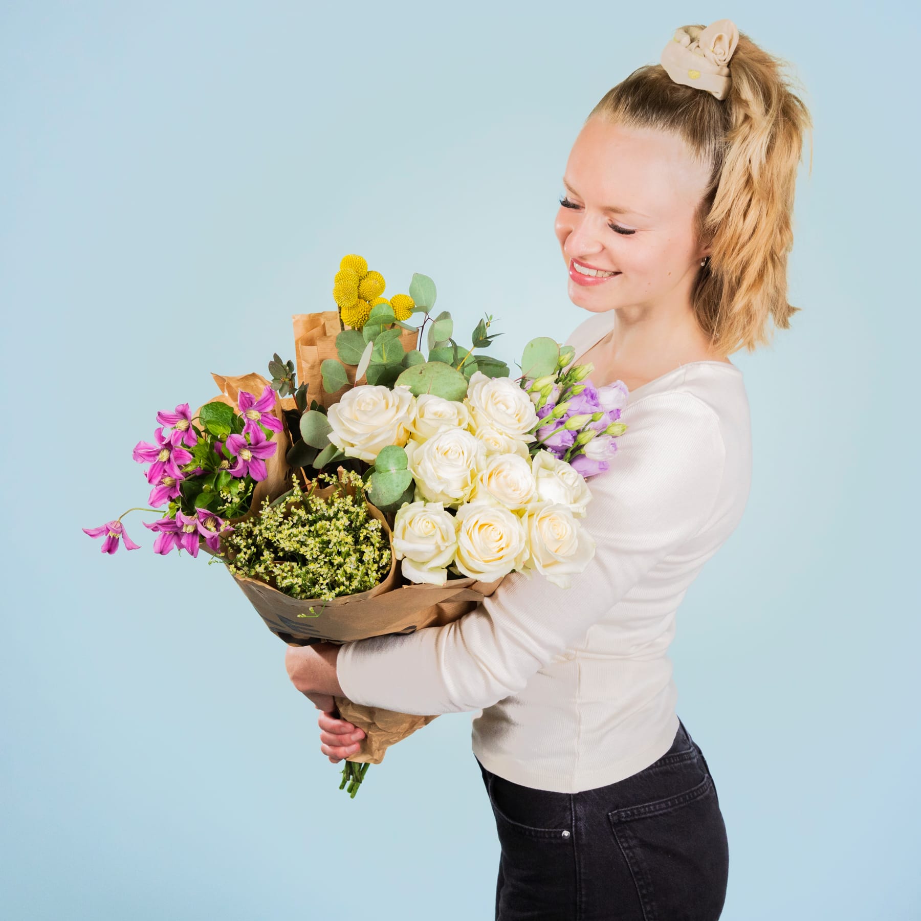 Eine lächelnde junge Frau hält einen leuchtend bunten Blumenstrauß vor einem schlichten blauen Hintergrund.
