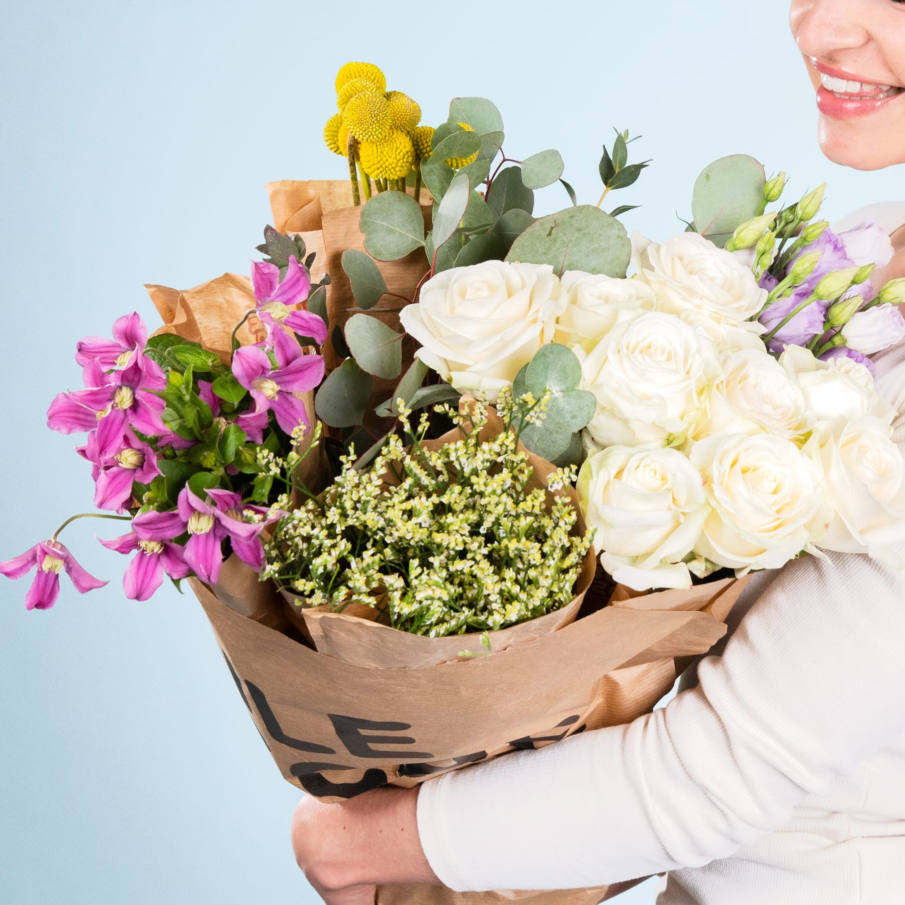 Ein Strauß leuchtender Blumen, darunter weiße Rosen, rosa Orchideen und gelbe Akzente, wird im Vordergrund vor einem schlichten blauen Hintergrund gehalten.