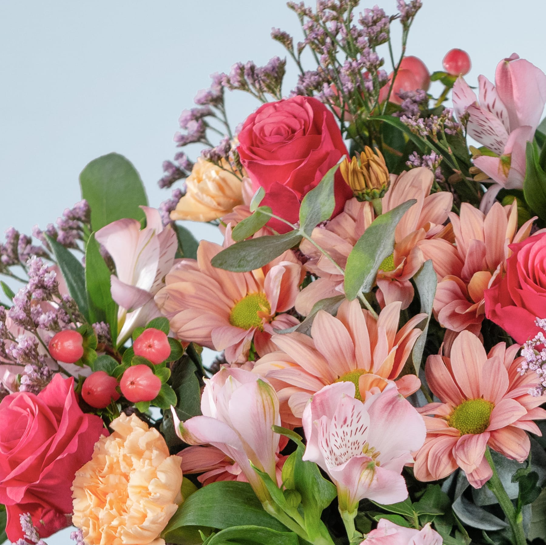 Ein lebendiger Strauß verschiedener bunter Blumen, darunter Rosen, Gänseblümchen und andere Blüten, vor einem klaren blauen Himmel im Hintergrund.
