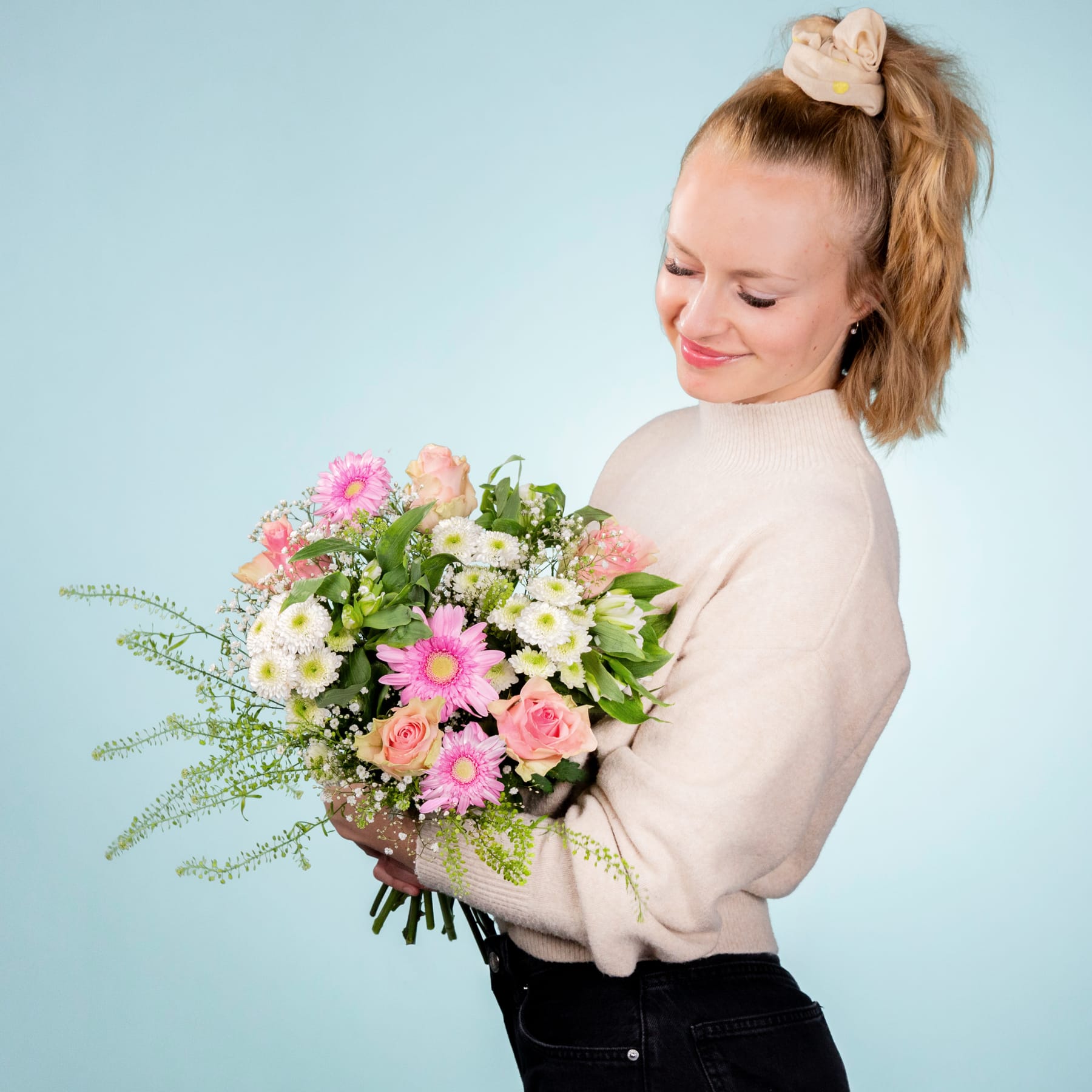 Eine junge Frau mit fröhlichem Gesichtsausdruck hält einen leuchtend bunten Blumenstrauß vor einem schlichten blauen Hintergrund.