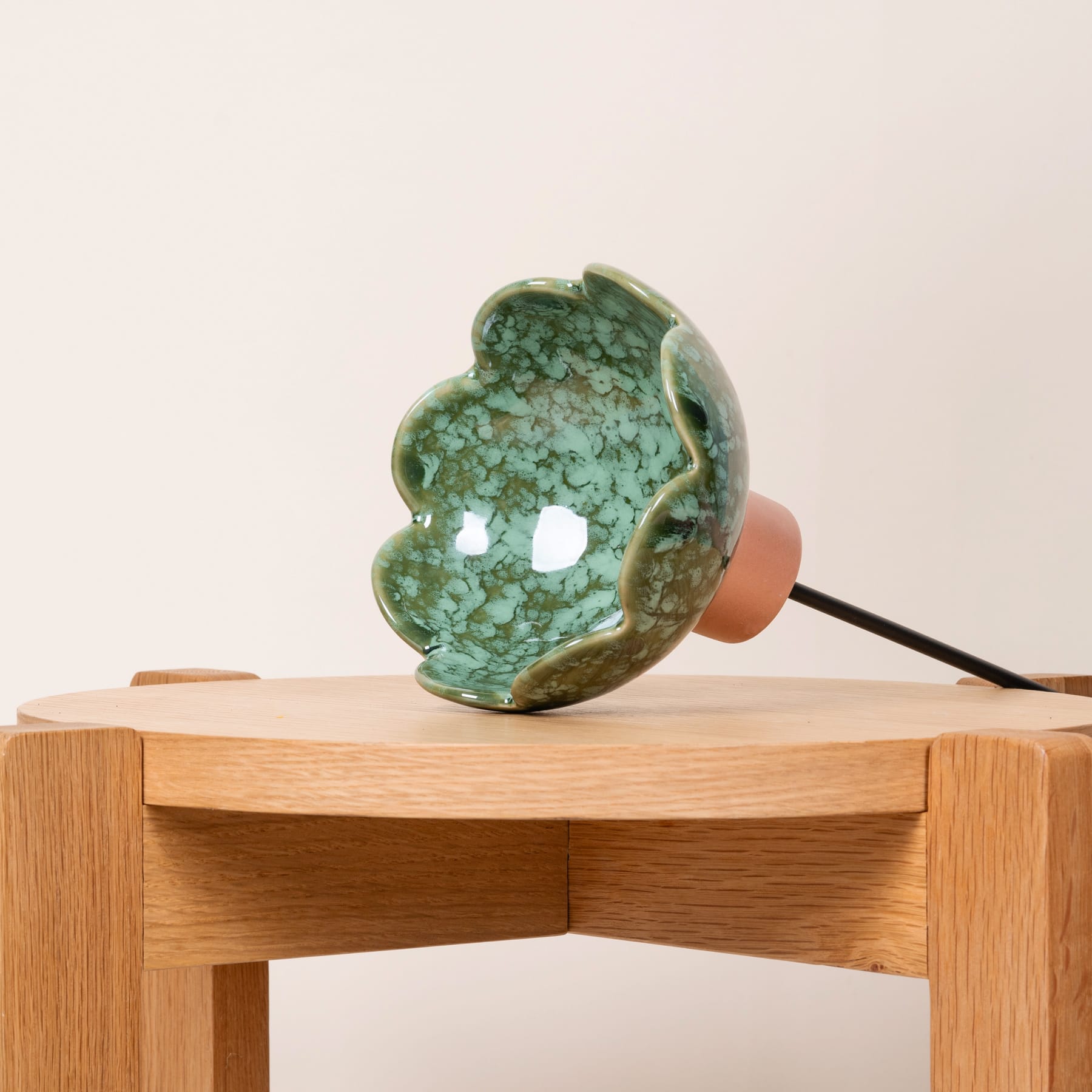 Eine grüne, kristalline Skulptur steht auf einem Holztisch vor einem schlichten, hellen Hintergrund.
