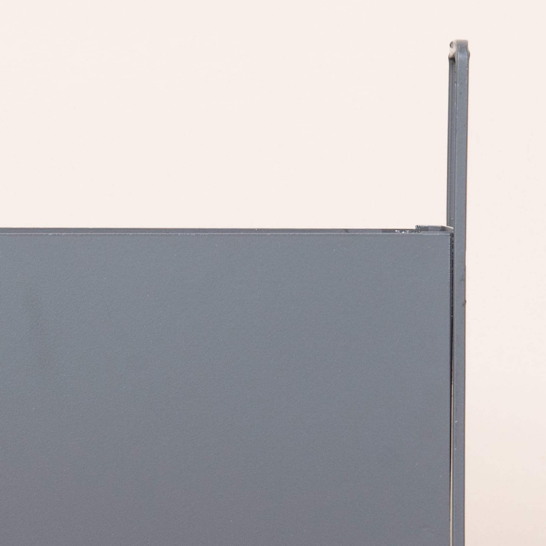 Vor einem hellen Hintergrund steht eine graue Metallplatte mit vertikaler Trägerstruktur.