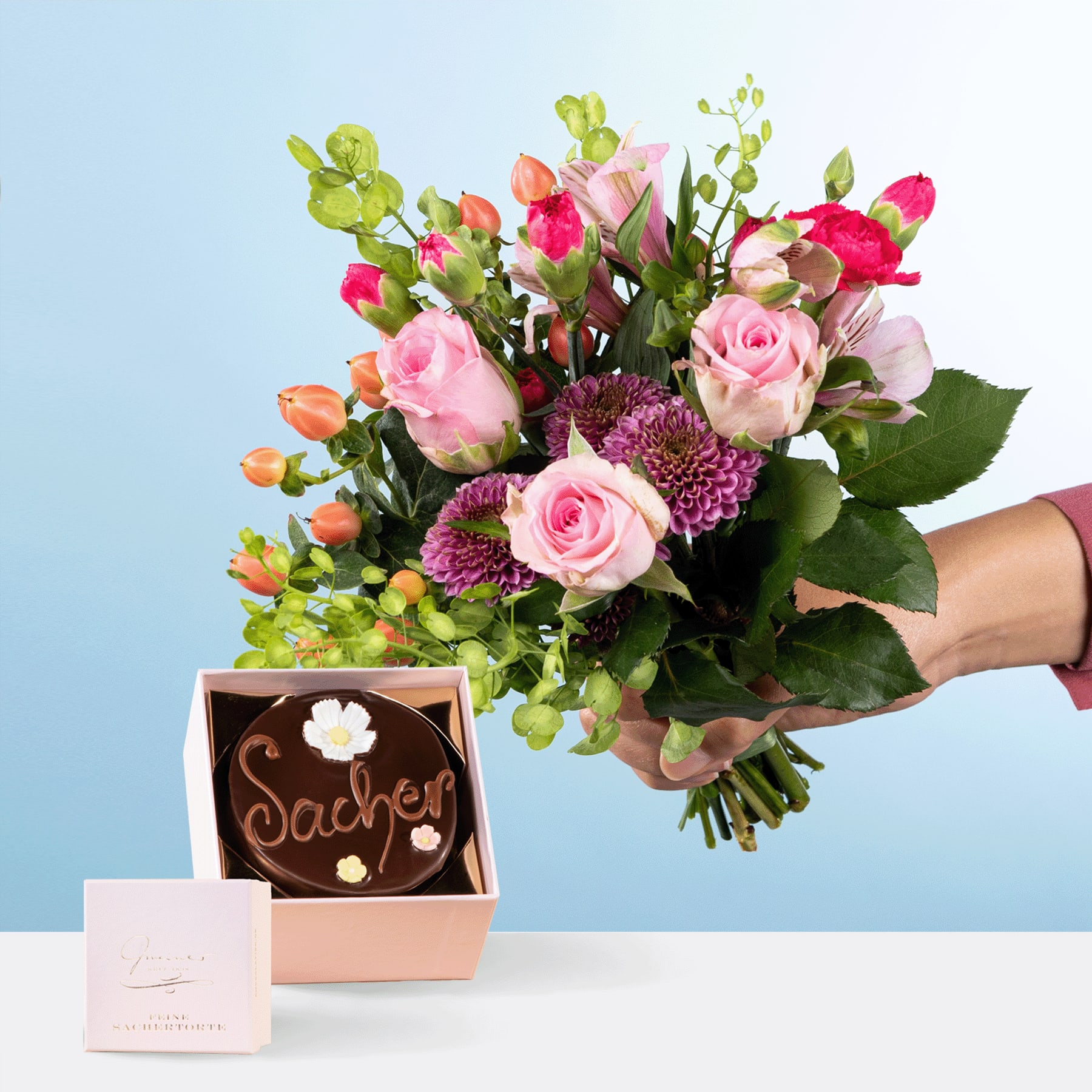Eine Person hält einen farbenfrohen Strauß rosa Rosen, violetter Chrysanthemen und grünem Laub in den Händen, begleitet von einer kleinen Geschenkbox mit der Aufschrift „Daddy“ auf hellblauem Hintergrund.