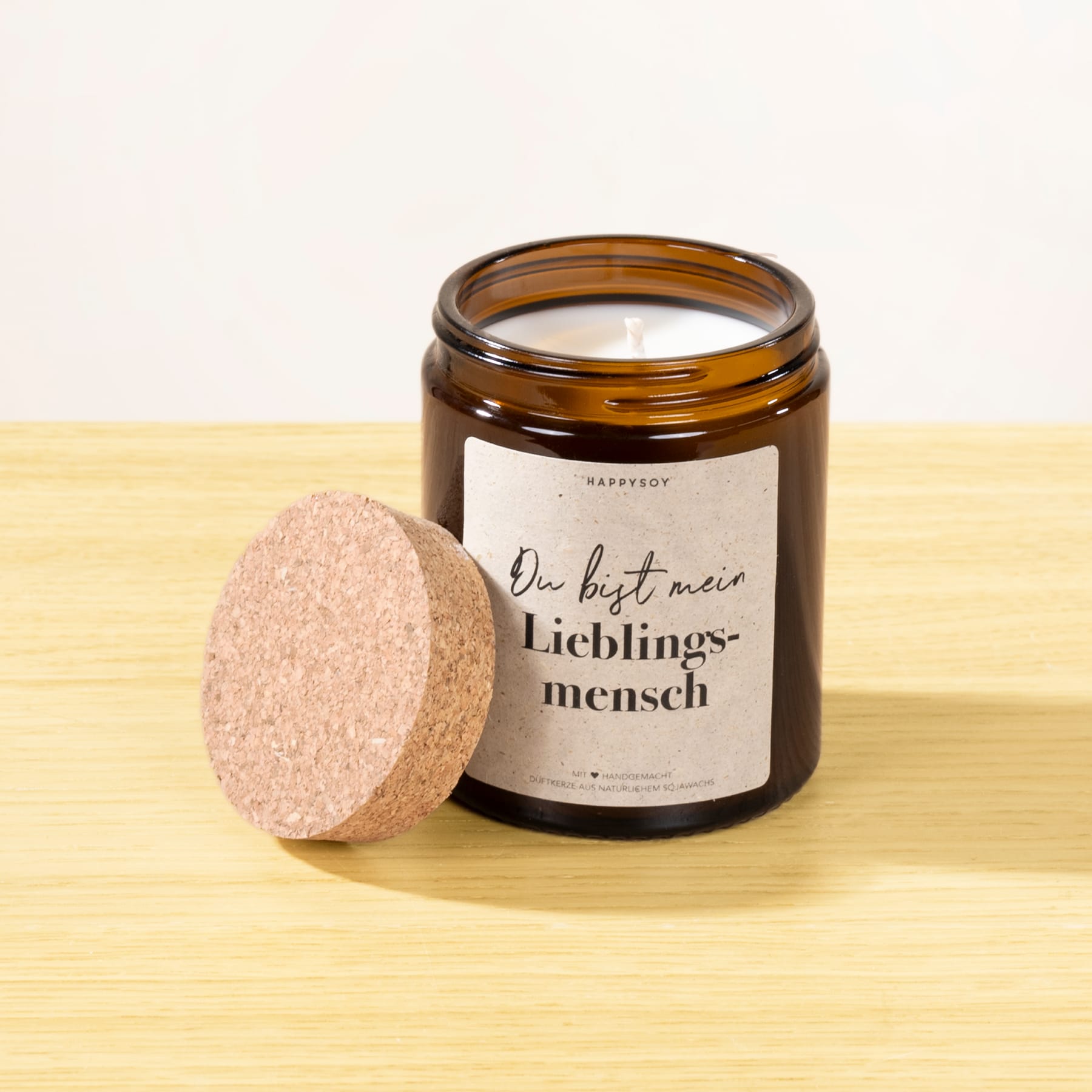 Auf einer Holzfläche steht ein Glasgefäß mit der Aufschrift „Der beste Mann, Lieblingsmench“, daneben ein runder, heller Gegenstand.