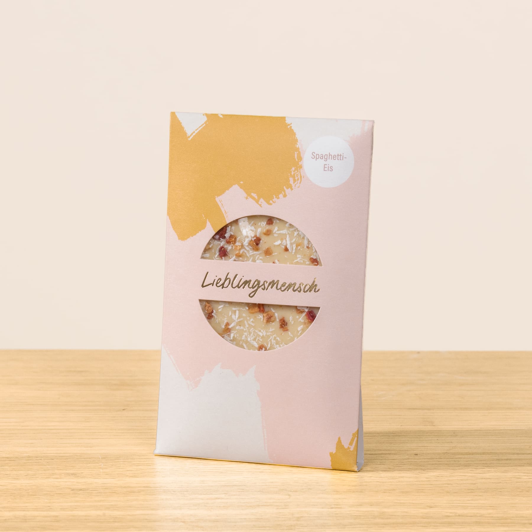 Eine rosa-weiße Verpackung mit einem runden Fenster zeigt eine Vielzahl getrockneter Blumen und Blütenblätter auf einer Holzoberfläche.