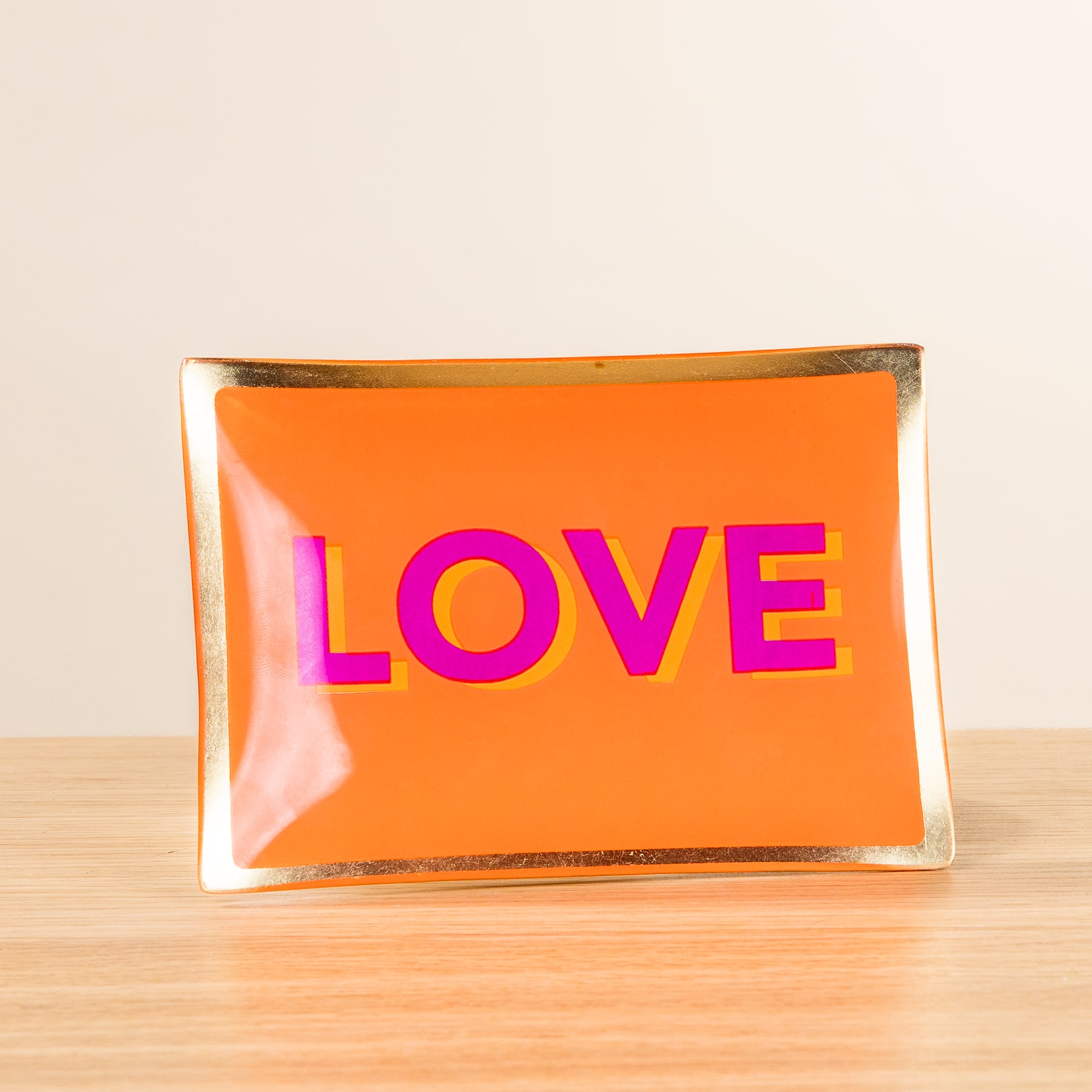 Auf einer Holzoberfläche steht eine transparente orangefarbene Box mit dem Wort „LOVE“ in großen rosa Buchstaben.