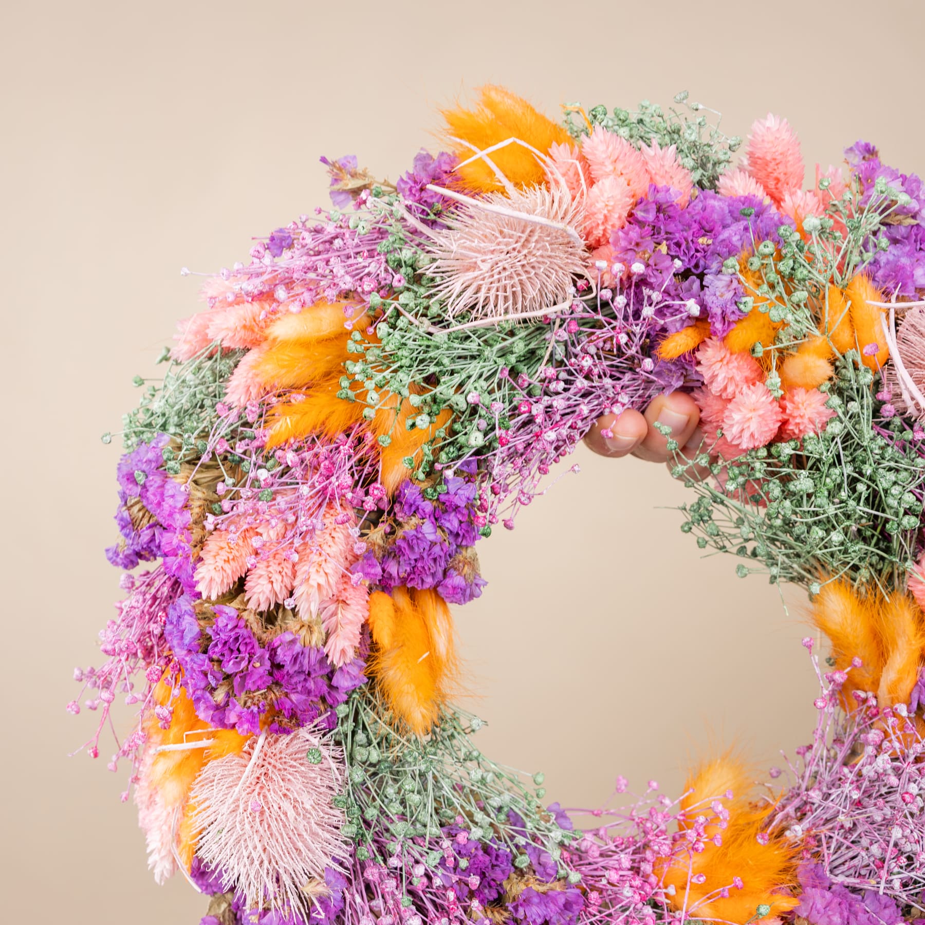 Ein lebendiger und farbenfroher Kranz aus verschiedenen Blumen, darunter violette, orangefarbene und rosa Blüten sowie Grünpflanzen, ziert die Mitte des Rahmens vor einem neutralen beigen Hintergrund.