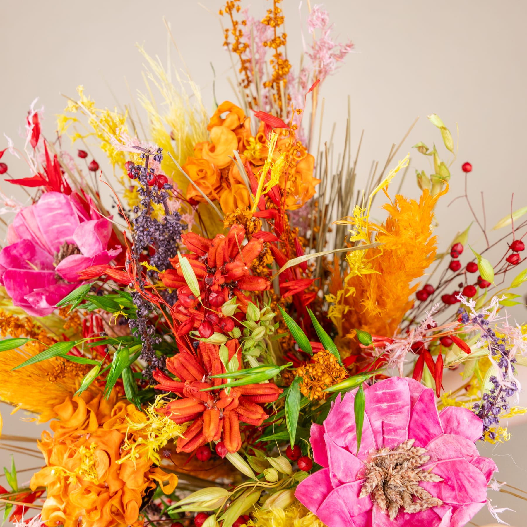 Ein lebendiger Strauß bunter Blumen, darunter rosa Pfingstrosen, orangefarbene Ringelblumen und verschiedene andere Blüten, arrangiert in einem rustikalen geflochtenen Korb vor einem neutralen Hintergrund.