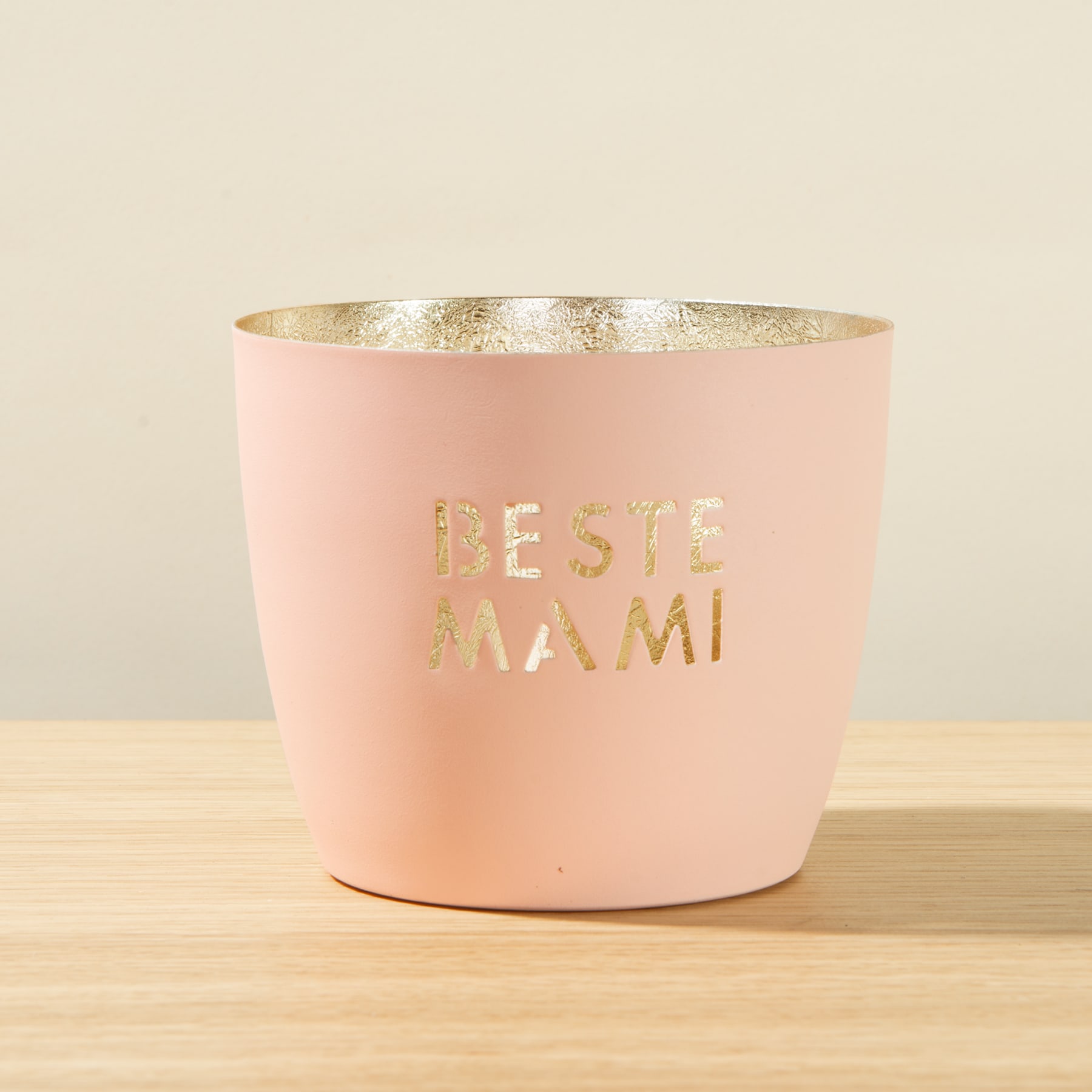 Ein rosa Behälter mit dem in Gold geschriebenen Text „BESTE MAMI“ (Beste Mama) auf einer Holzoberfläche.