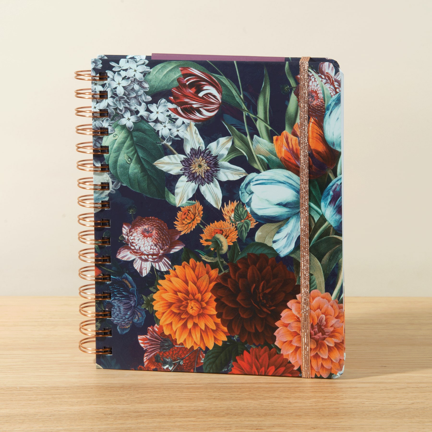 Ein lebendiges und üppiges Blumenmuster ziert den Einband eines Spiralnotizbuchs und zeigt eine Mischung aus bunten Blüten, darunter Dahlien, Narzissen und andere leuchtende Blumen vor einem dunklen Hintergrund.
