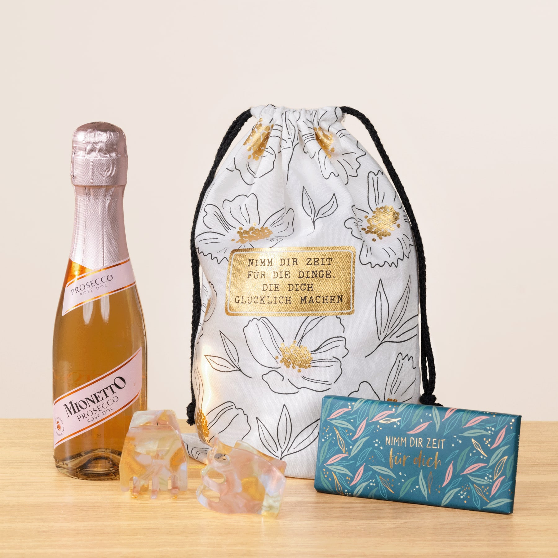Eine Flasche Moscato-Wein, ein Beutel mit Blumenmuster und eine Schachtel Gummibonbons sind auf einer Holzoberfläche vor einem schlichten Hintergrund angeordnet.