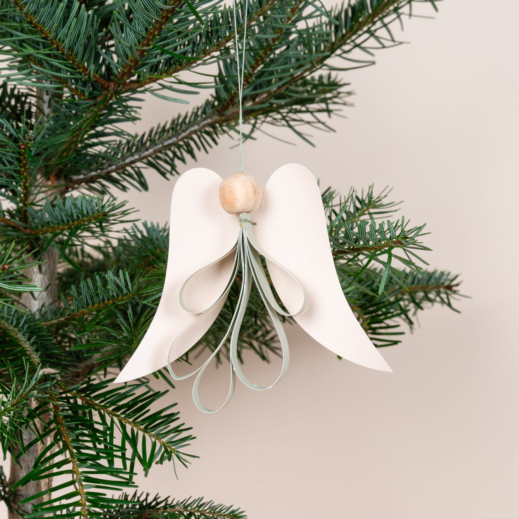 Ein weißer Engel aus Papier hängt an einem üppigen, grünen Weihnachtsbaum. Seine zarten Flügel und sein Heiligenschein schaffen eine heitere und festliche Szene.
