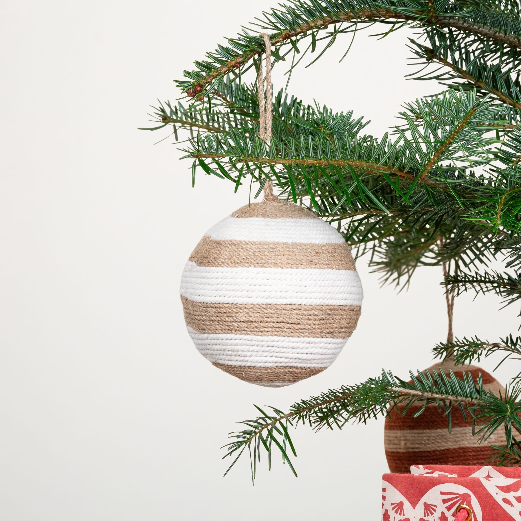 Vor einem schlichten weißen Hintergrund hängt ein mit einem gestreiften Ornament geschmückter Weihnachtsbaum.