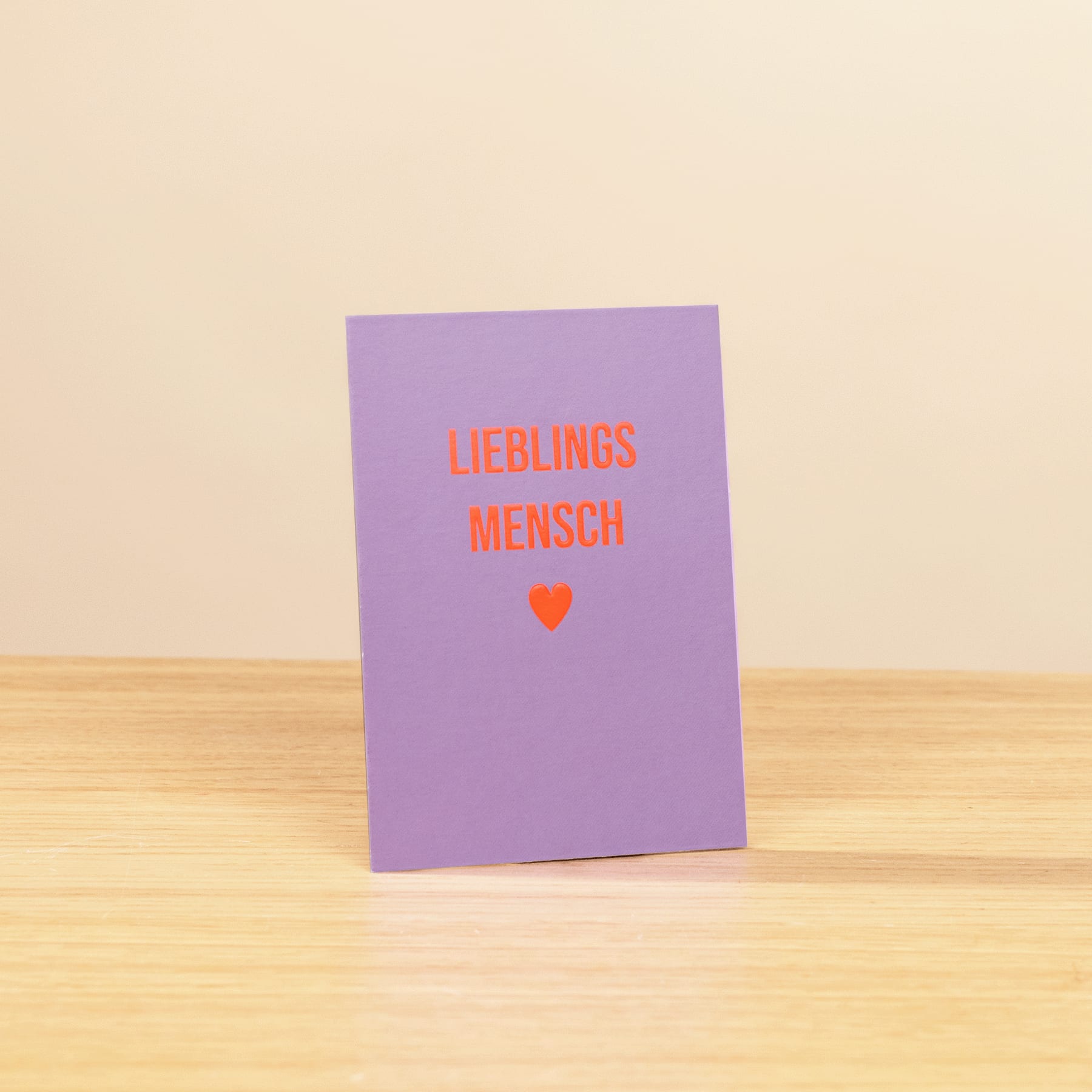 Eine lila Karte mit dem Text „LIEBLINGSMENCH“ in Rot auf einer Holzoberfläche.