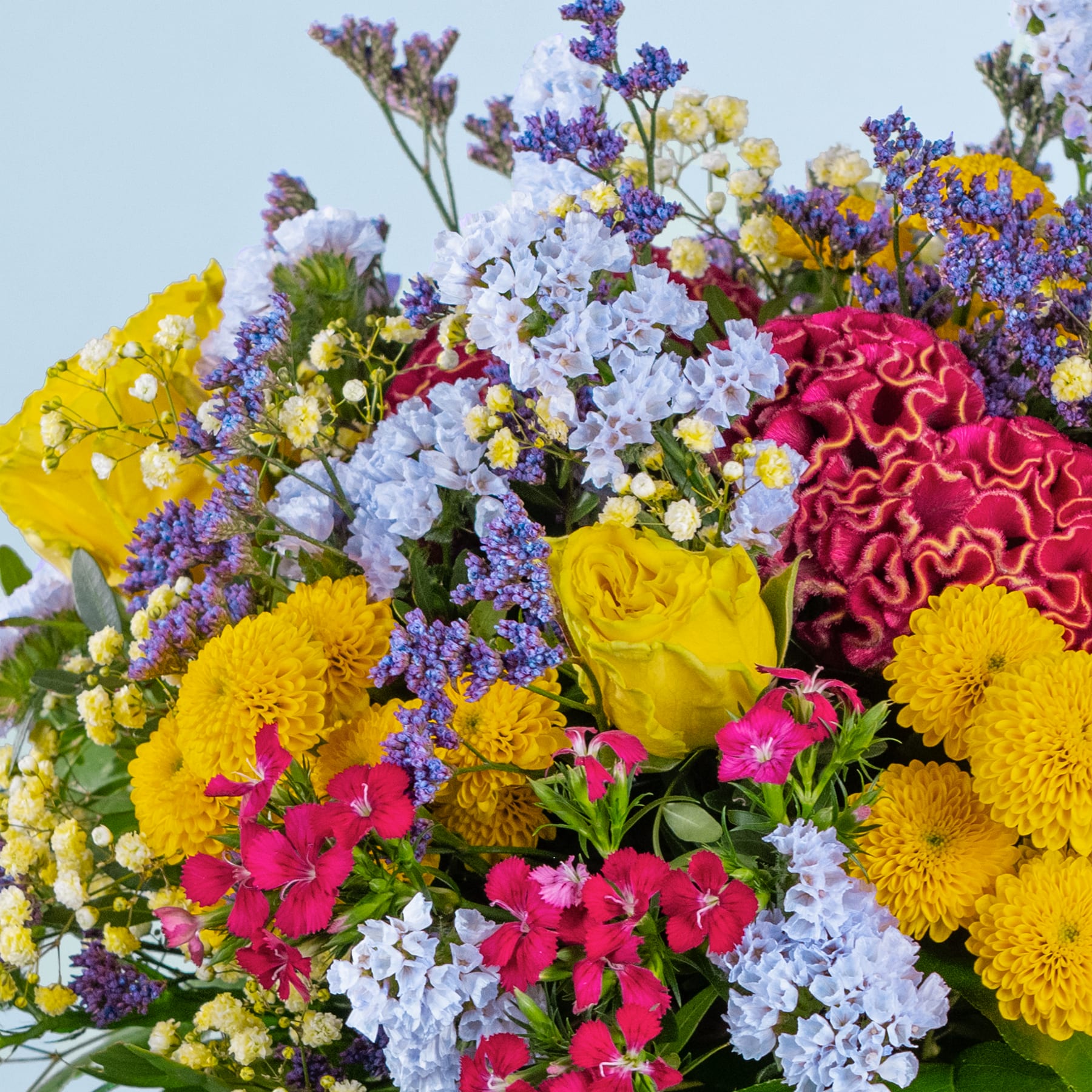 Ein lebendiger und farbenfroher Strauß verschiedener Blumen, darunter gelbe Chrysanthemen, rosa Nelken und violette und weiße Blüten, vor einem sanften blauen Hintergrund.