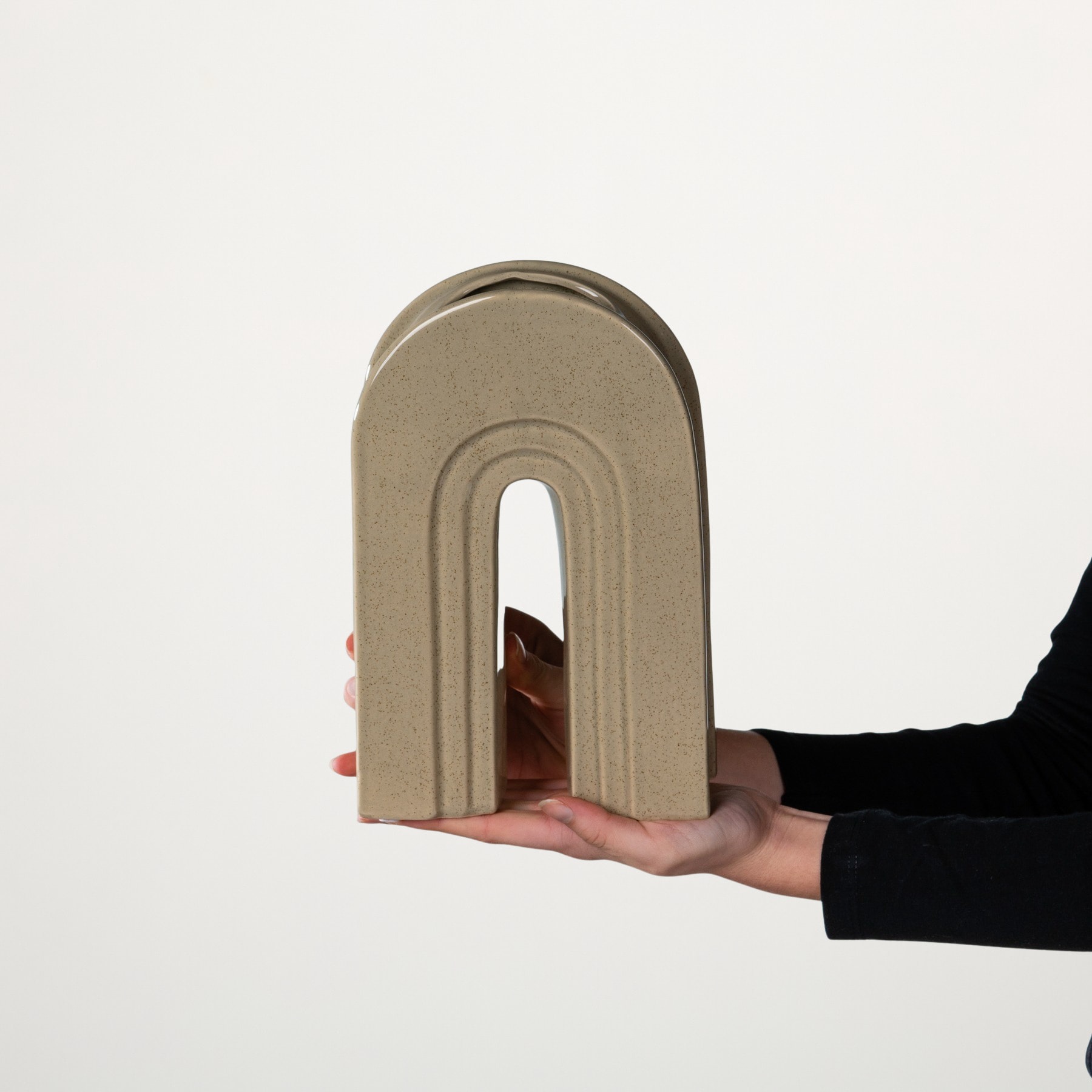 Eine Hand hält ein großes, gewölbtes, beigefarbenes Objekt vor einem schlichten weißen Hintergrund.