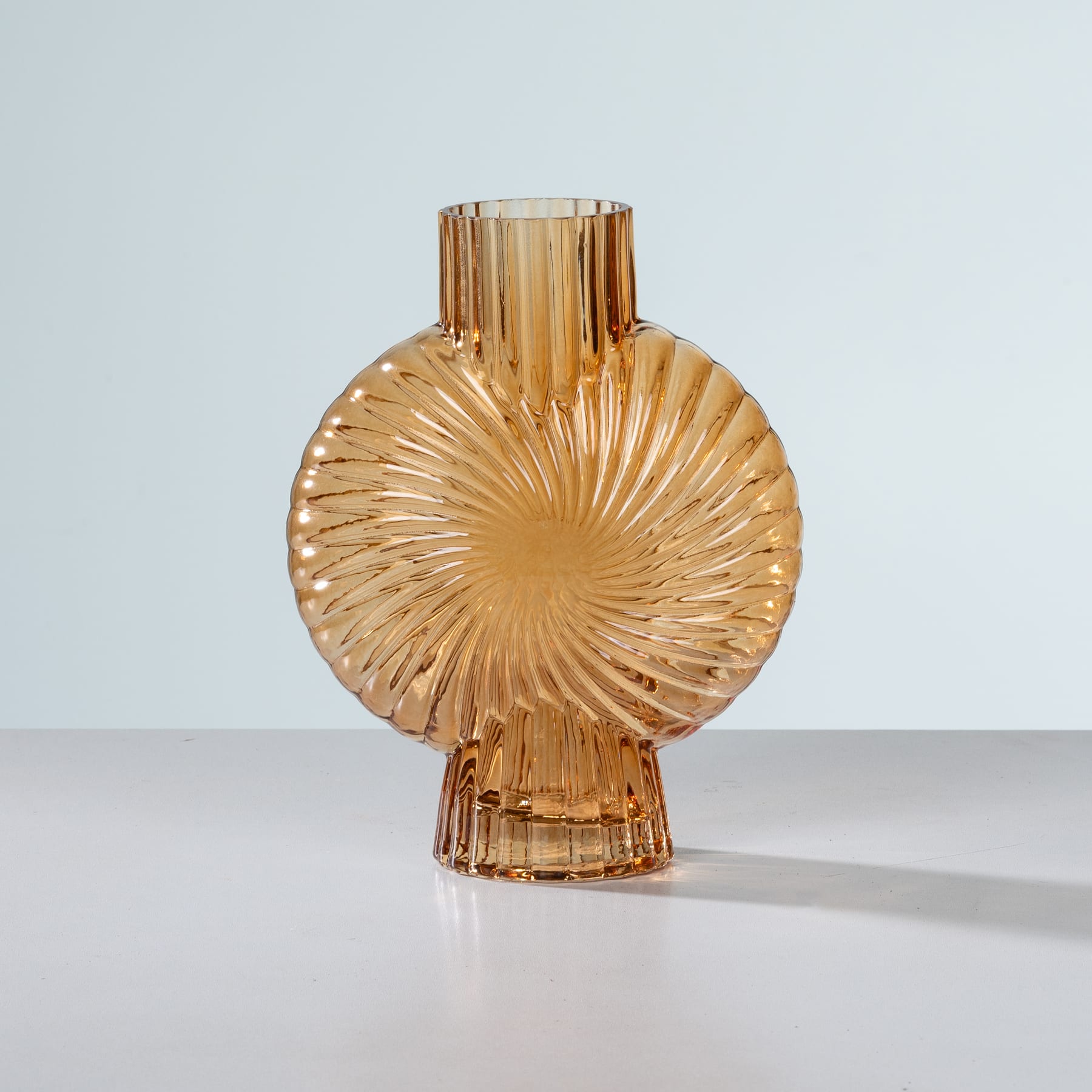Eine goldene, gerippte Glasvase mit einem einzigartigen, radialen Design steht auf einer schlichten, hellen Oberfläche vor einem neutralen Hintergrund.