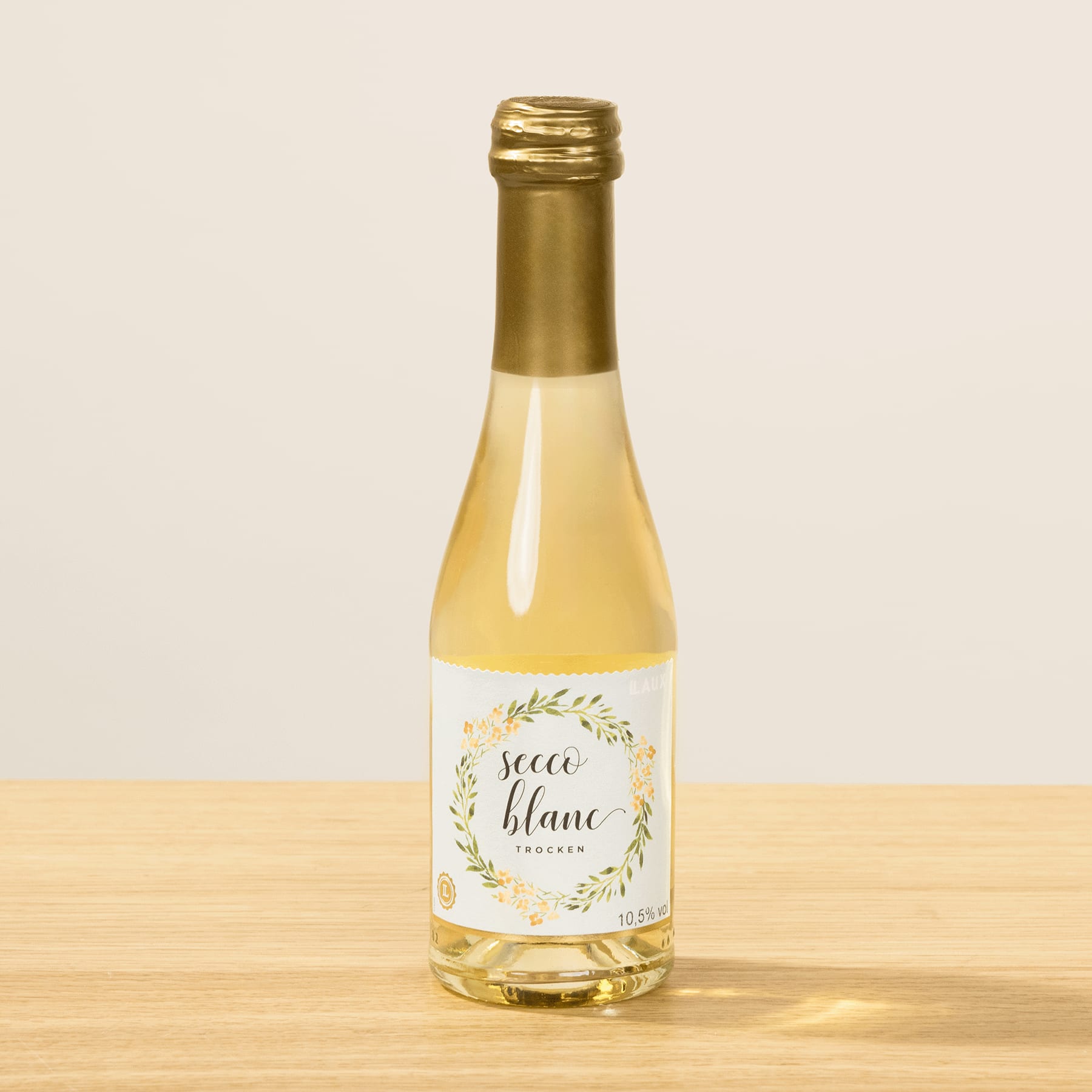 Eine Glasflasche Weißwein mit goldenem Verschluss steht auf einer Holzoberfläche vor einem schlichten Hintergrund.