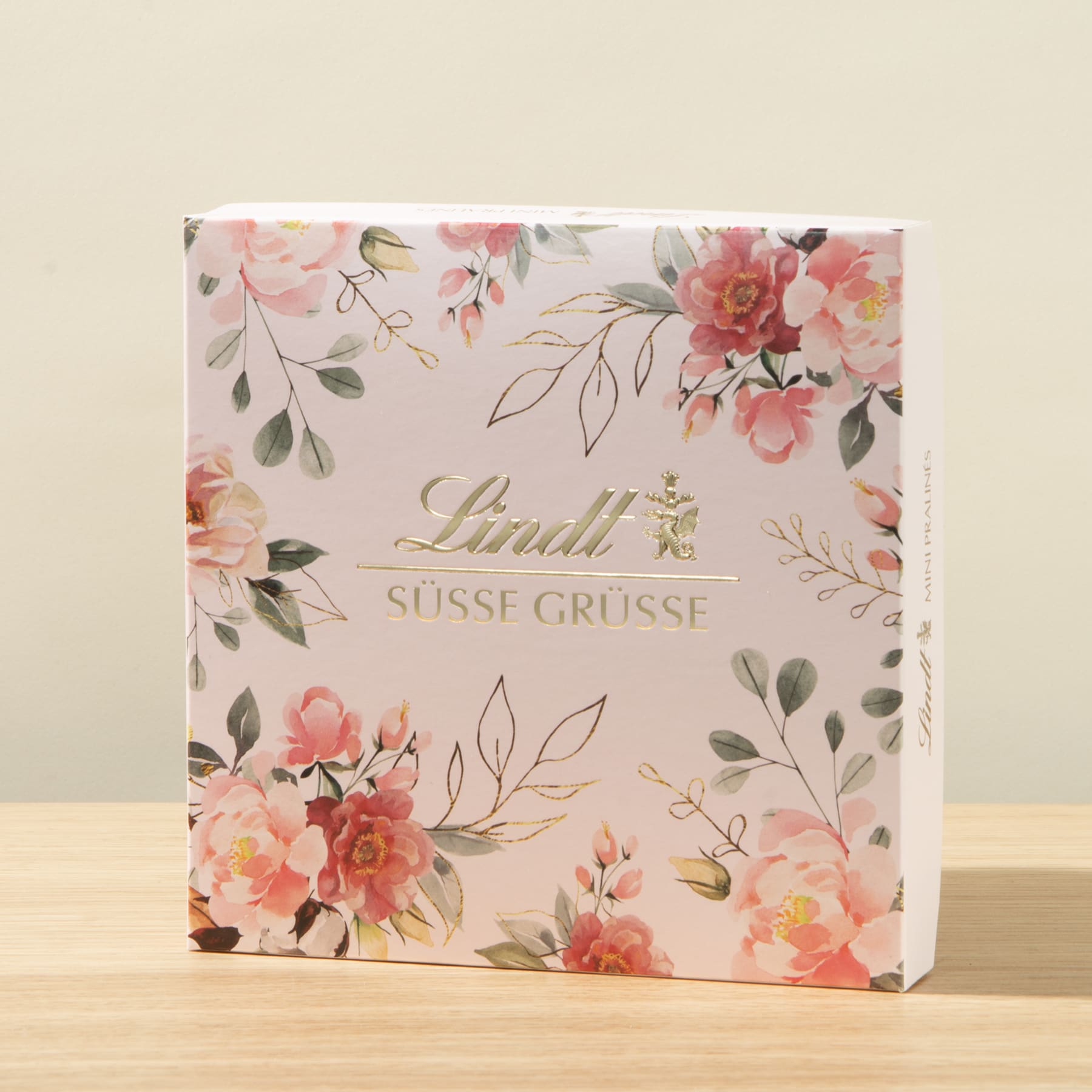 Eine quadratische Geschenkbox mit einem Blumenmuster aus rosa und weißen Blumen auf hellem Hintergrund.
