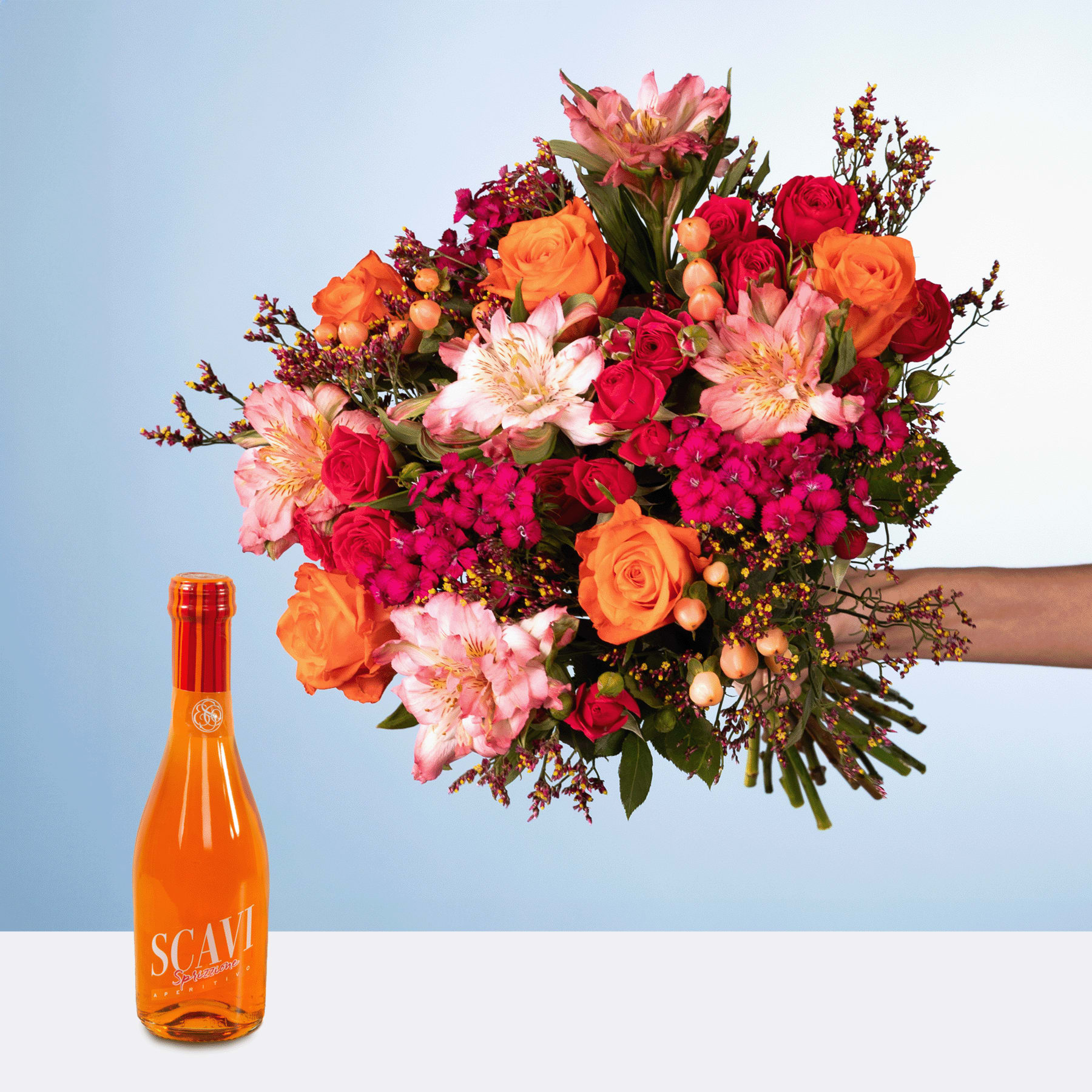 Ein farbenfroher Strauß roter, orangefarbener und rosa Blumen, darunter Rosen und Dahlien, wird neben einer orangefarbenen Flasche Scavi-Wein vor einem schlichten blauen Hintergrund präsentiert.