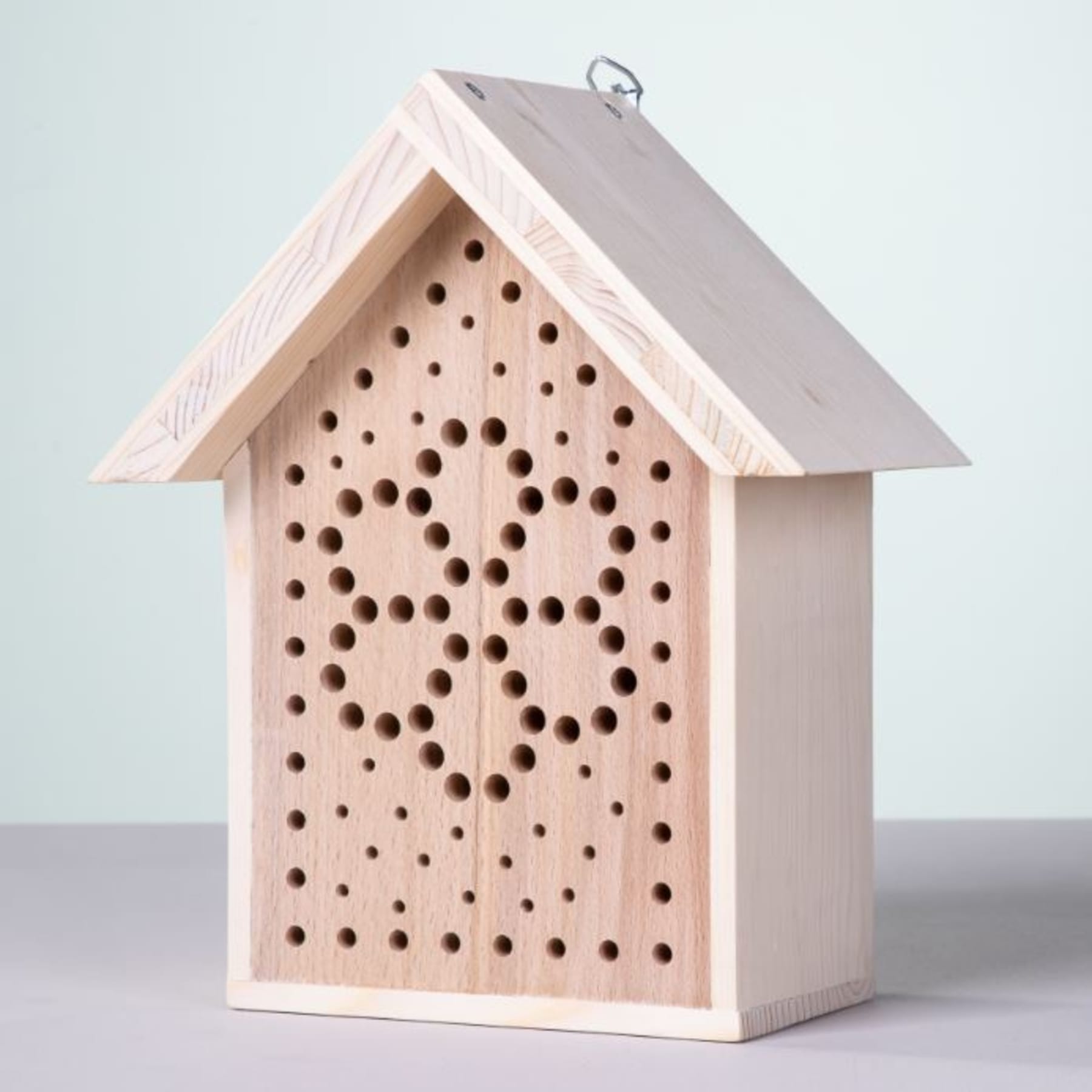 Ein Insektenhotel aus Holz mit schrägem Dach und zahlreichen Löchern, in denen Insekten Schutz und Nistmöglichkeiten finden.