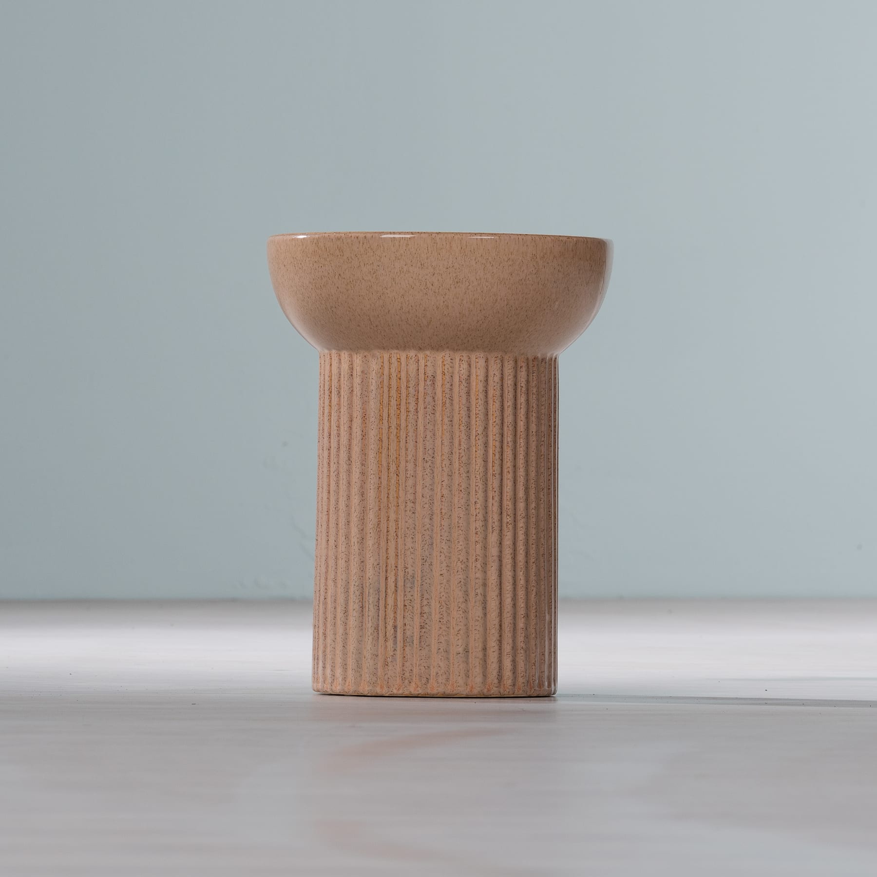 Auf einer schlichten, hellen Oberfläche steht ein hölzernes, sockelartiges Objekt mit einer flachen, schüsselförmigen Oberseite.