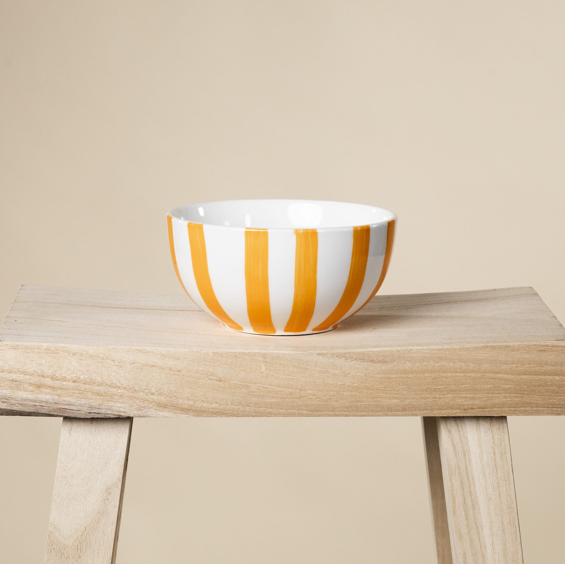 Eine weiß und orange gestreifte Keramikschale steht auf einem Holztisch vor einem beigen Hintergrund.