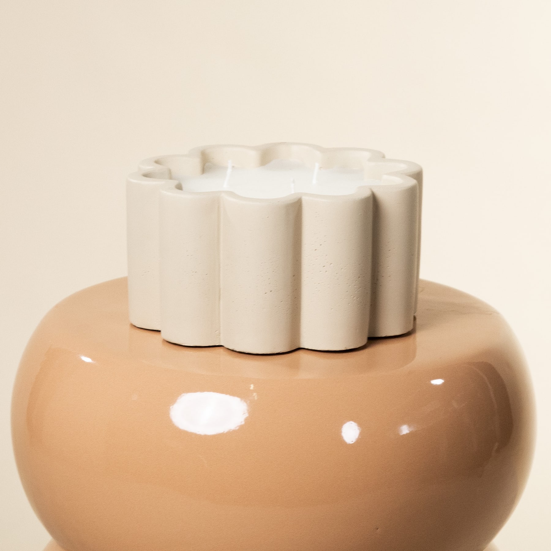 Eine runde, beige Keramikvase mit gewelltem Rand steht auf einer schlichten, hellen Oberfläche.