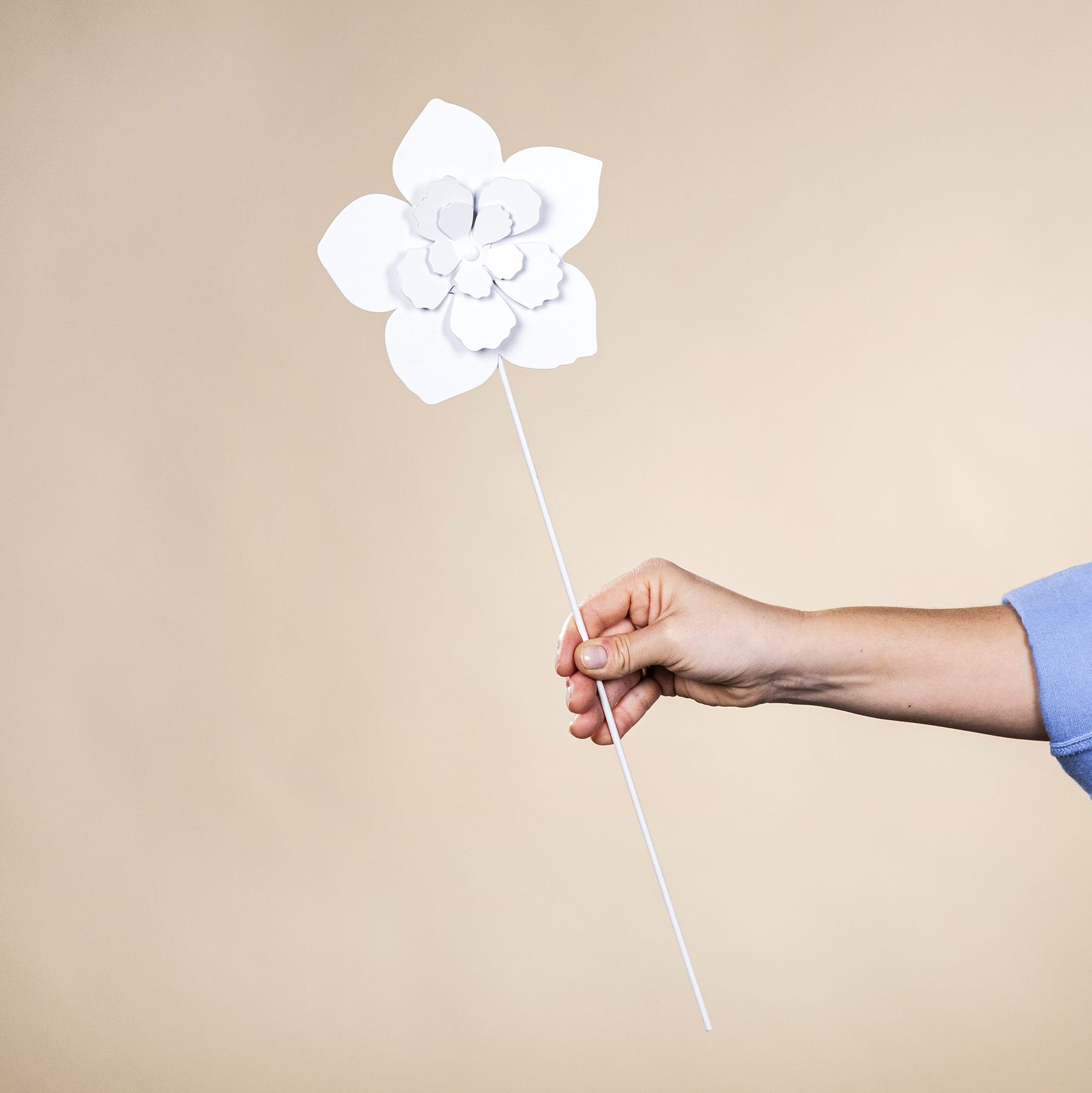 Eine große weiße Papierblume wird vor einem beigen Hintergrund in einer Hand gehalten.