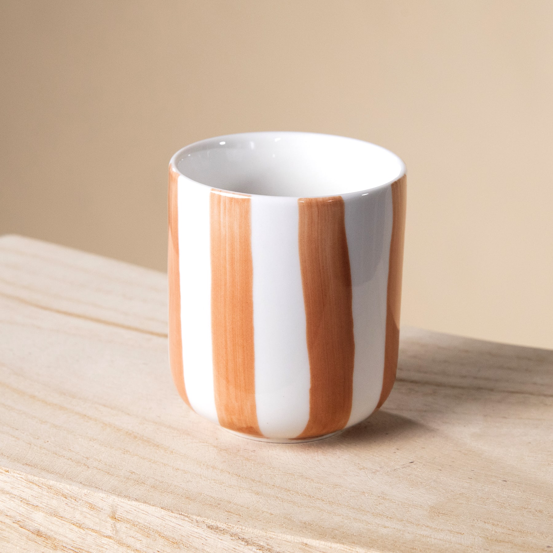 Eine weiß-orangefarbene Keramiktasse steht auf einer Holzoberfläche vor einem beigen Hintergrund.
