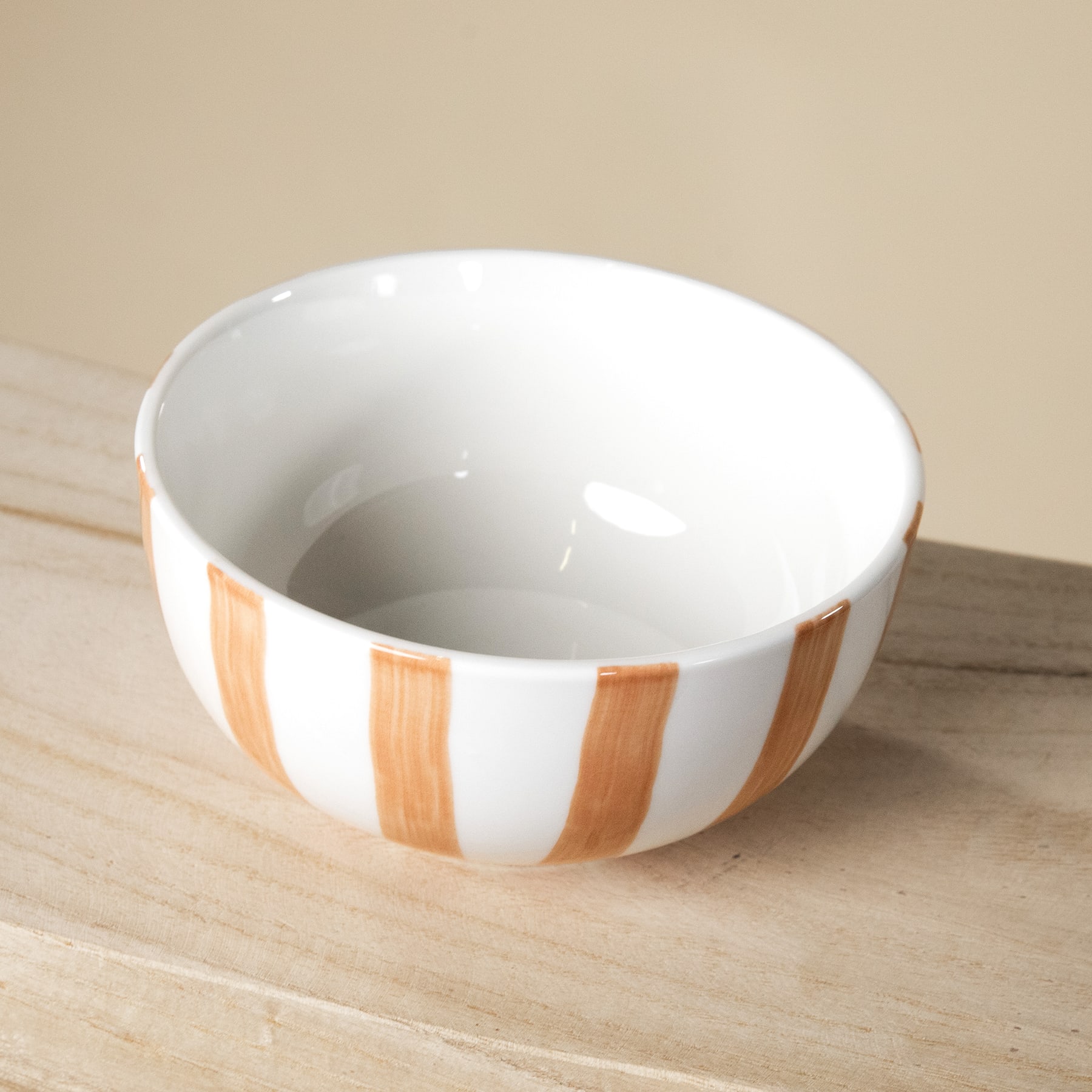 Eine weiße Keramikschale mit orange-weißem Streifenmuster steht auf einer Holzoberfläche.