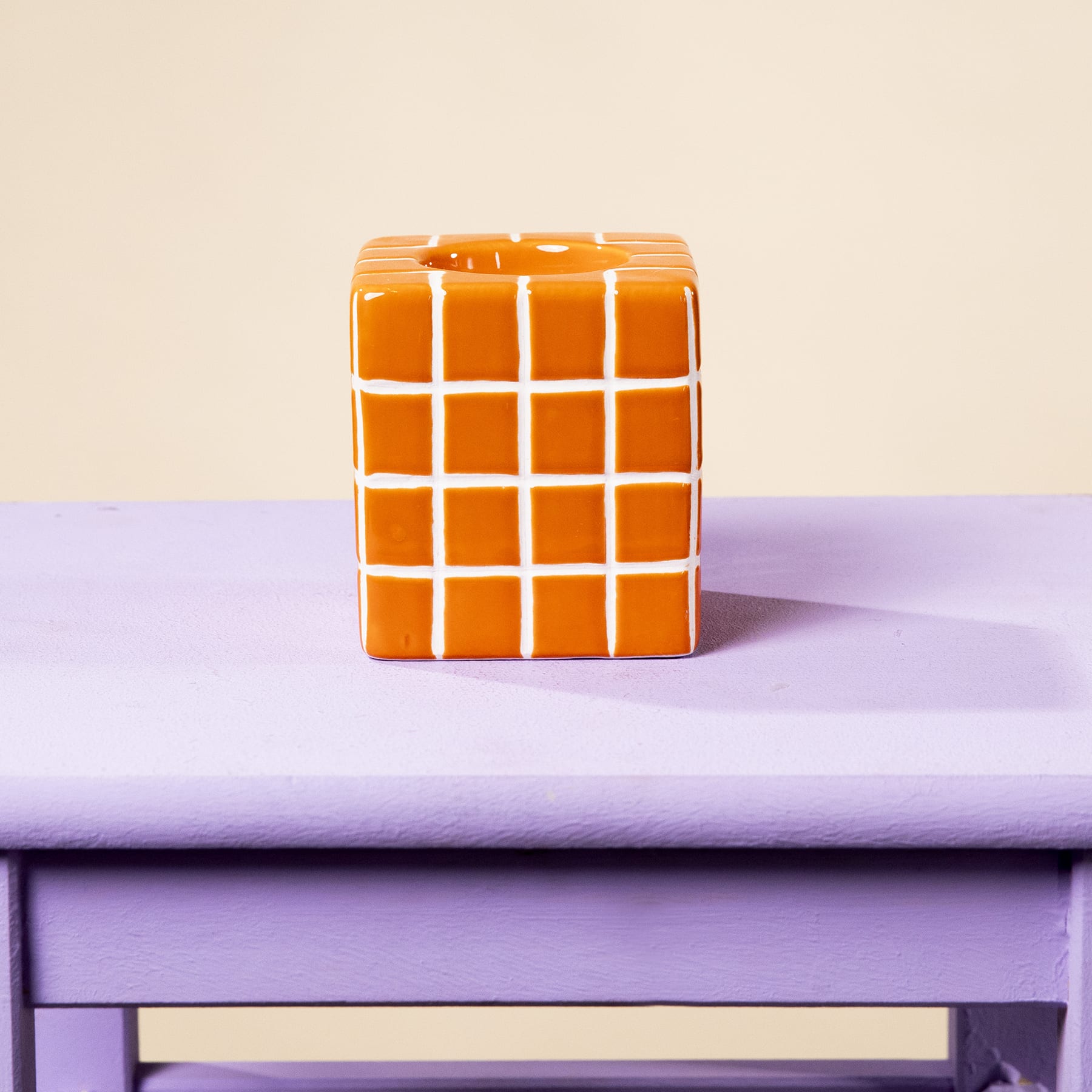 Ein leuchtend orangefarbenes Puzzle in der Art eines Zauberwürfels liegt auf einer lavendelfarbenen Holzoberfläche vor einem schlichten beigen Hintergrund.
