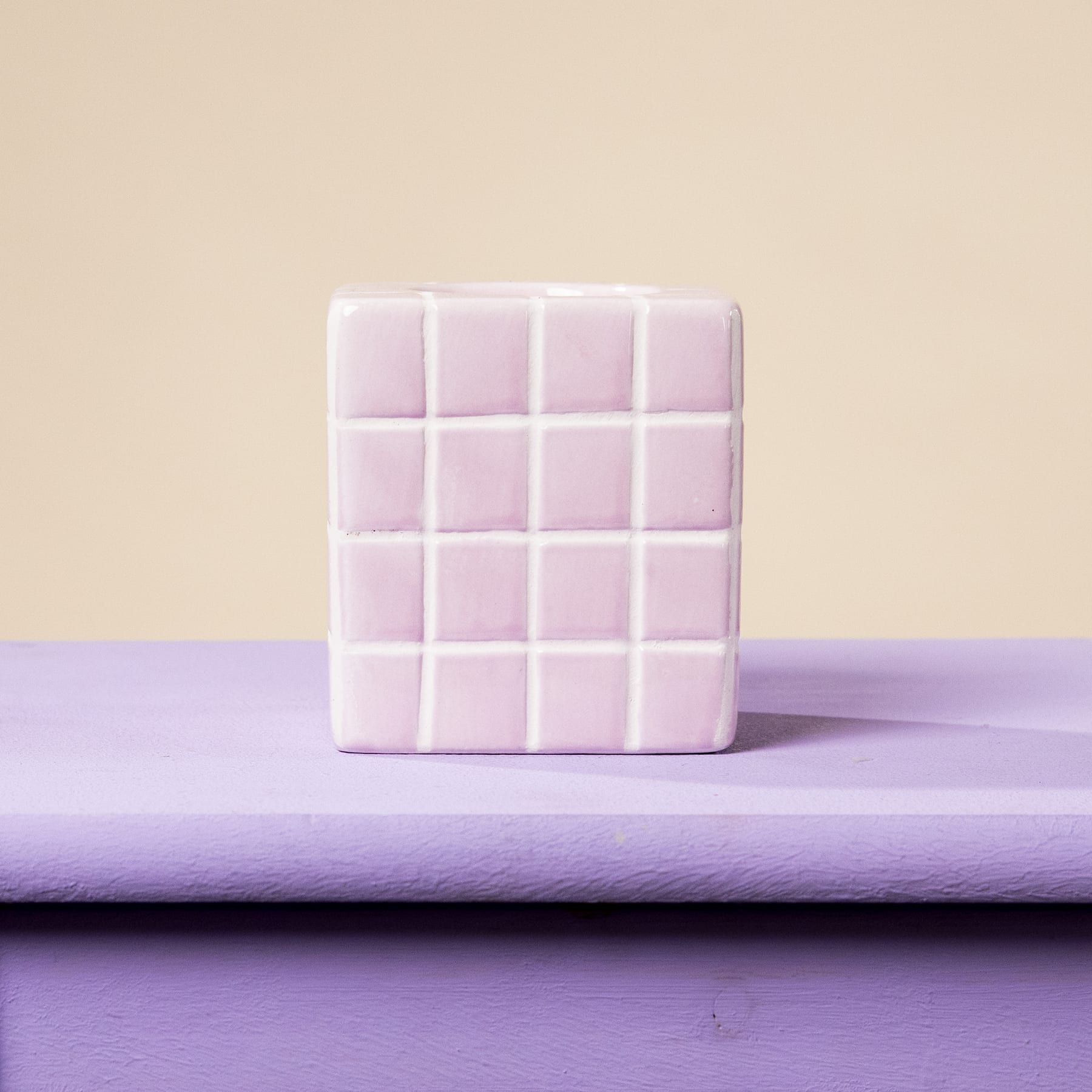 Ein weißes, würfelförmiges Objekt mit einem Gittermuster liegt auf einer violetten Oberfläche vor einem beigen Hintergrund.