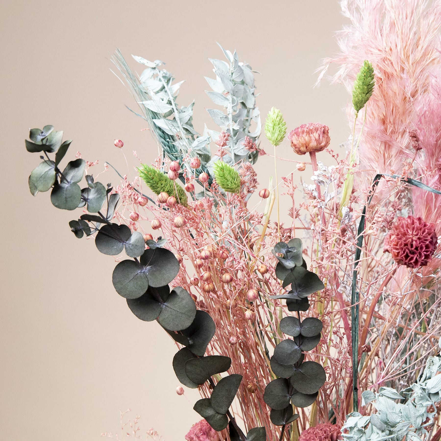 Ein lebendiger Strauß verschiedener Blumen, darunter rosa Dahlien, Eukalyptusblätter und zarte weiße Blüten, vor einem weichen, neutralen Hintergrund.