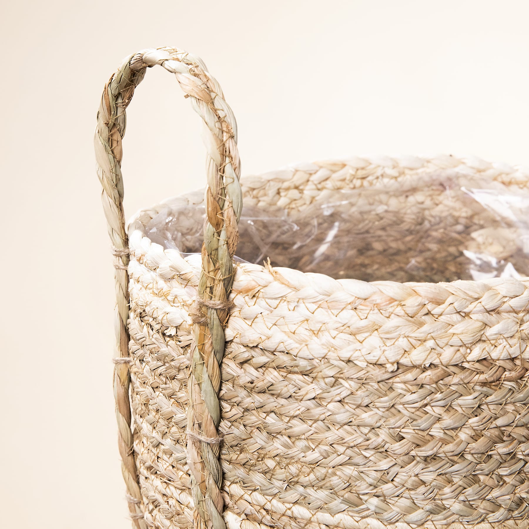 Auf einer schlichten, hellen Fläche steht ein geflochtener Strohkorb mit geschwungenem Henkel.