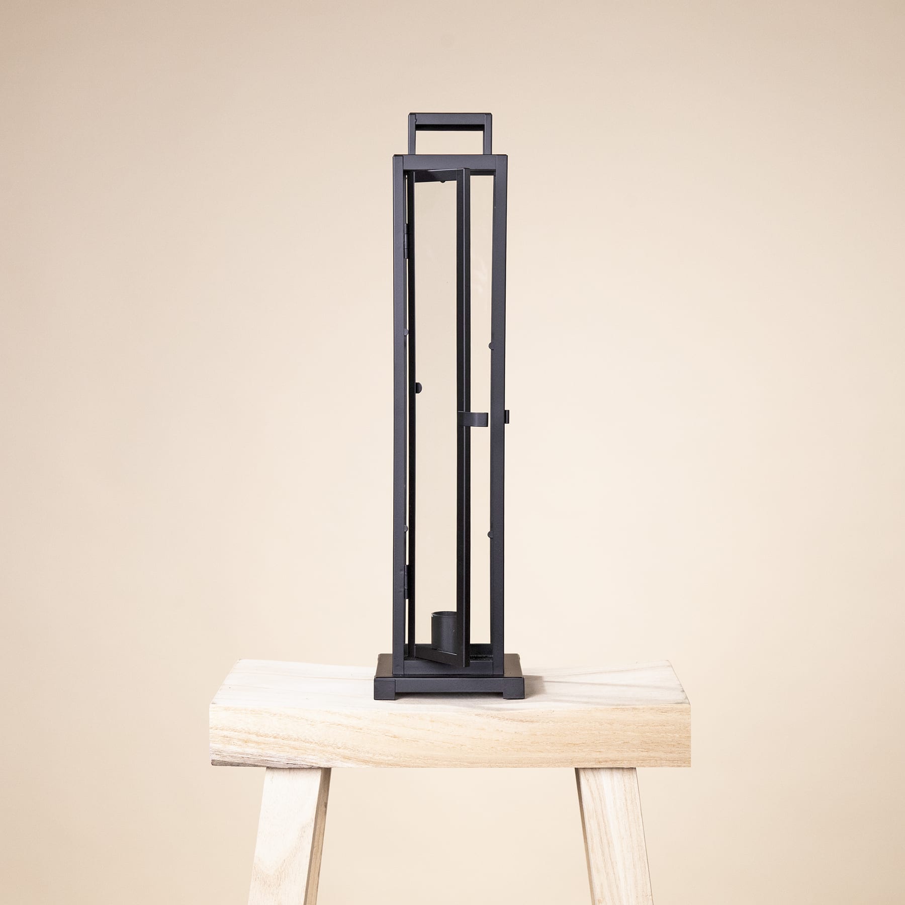 Vor einem schlichten beigen Hintergrund steht eine schwarze Metallrahmenkonstruktion auf einem Holzhocker.