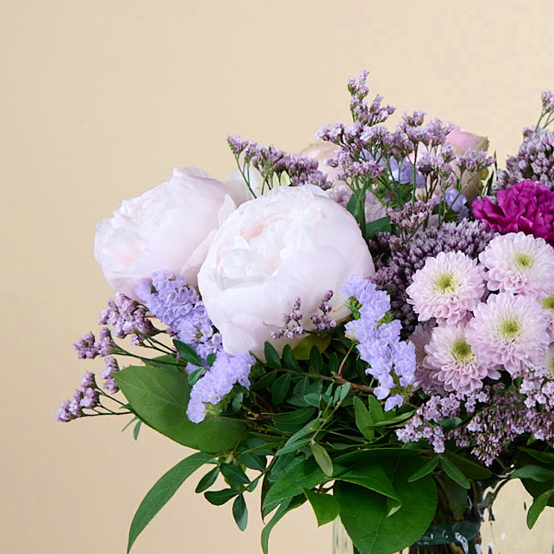 Ein lebendiger Strauß weißer und violetter Blumen, darunter Pfingstrosen und Chrysanthemen, vor einem sanften, beigen Hintergrund.