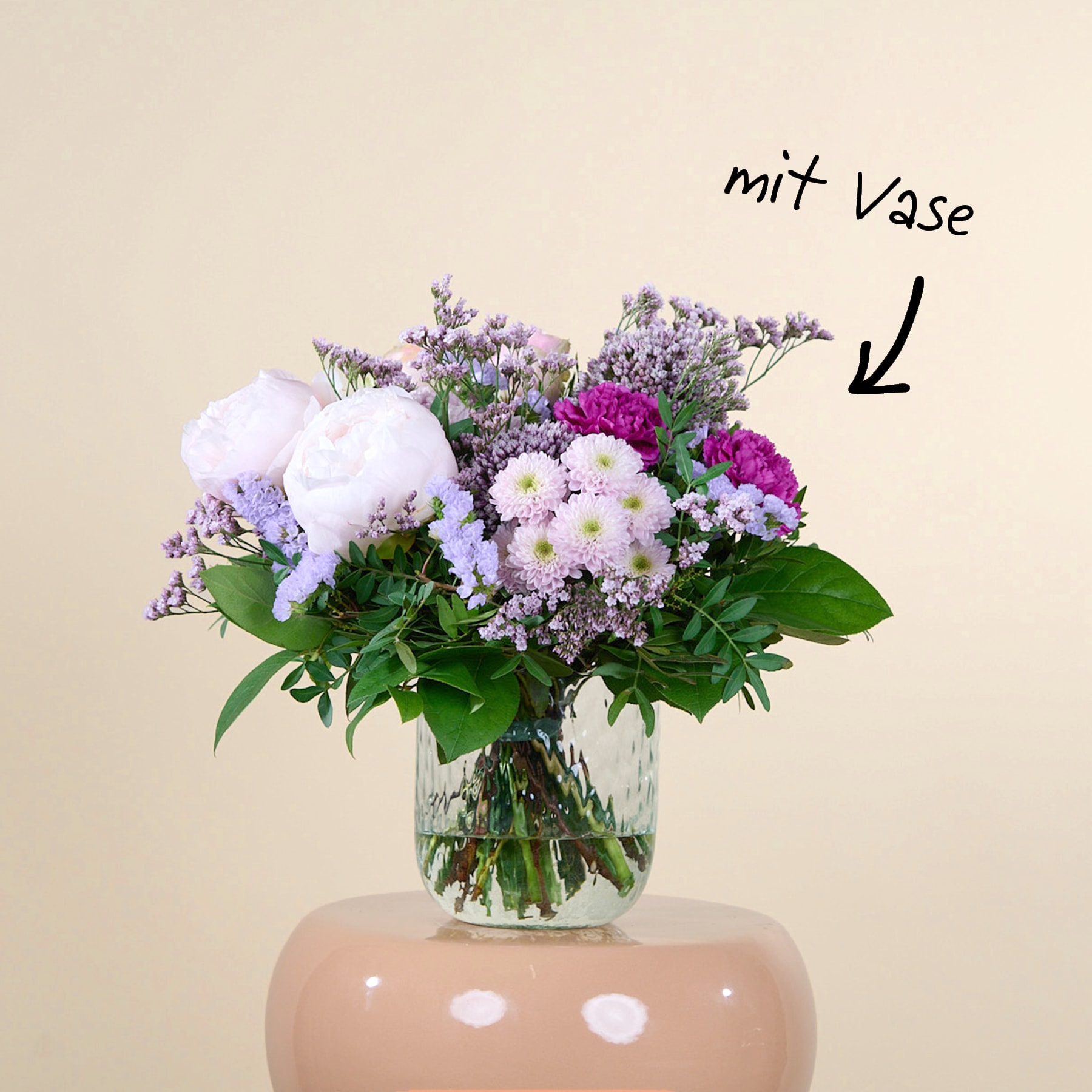 Ein Strauß leuchtend violetter und rosa Blumen, darunter Pfingstrosen und andere Blüten, wird in einer Glasvase vor einem schlichten beigen Hintergrund präsentiert.